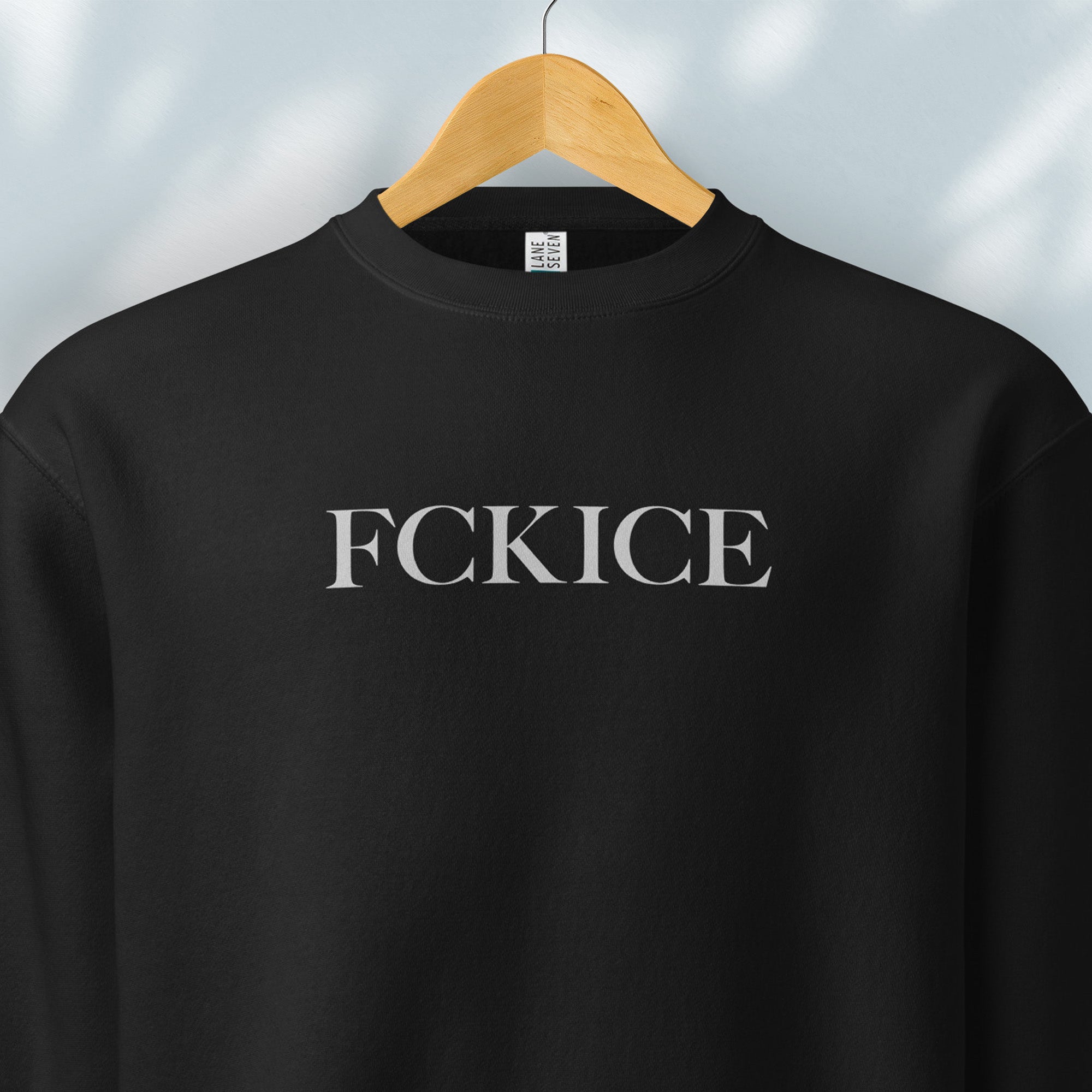Hanging black sweatshirt with minimalist serif typography reading “FCK ICE,” an anti-ICE political message opposing Immigration and Customs Enforcement abuses and violence.