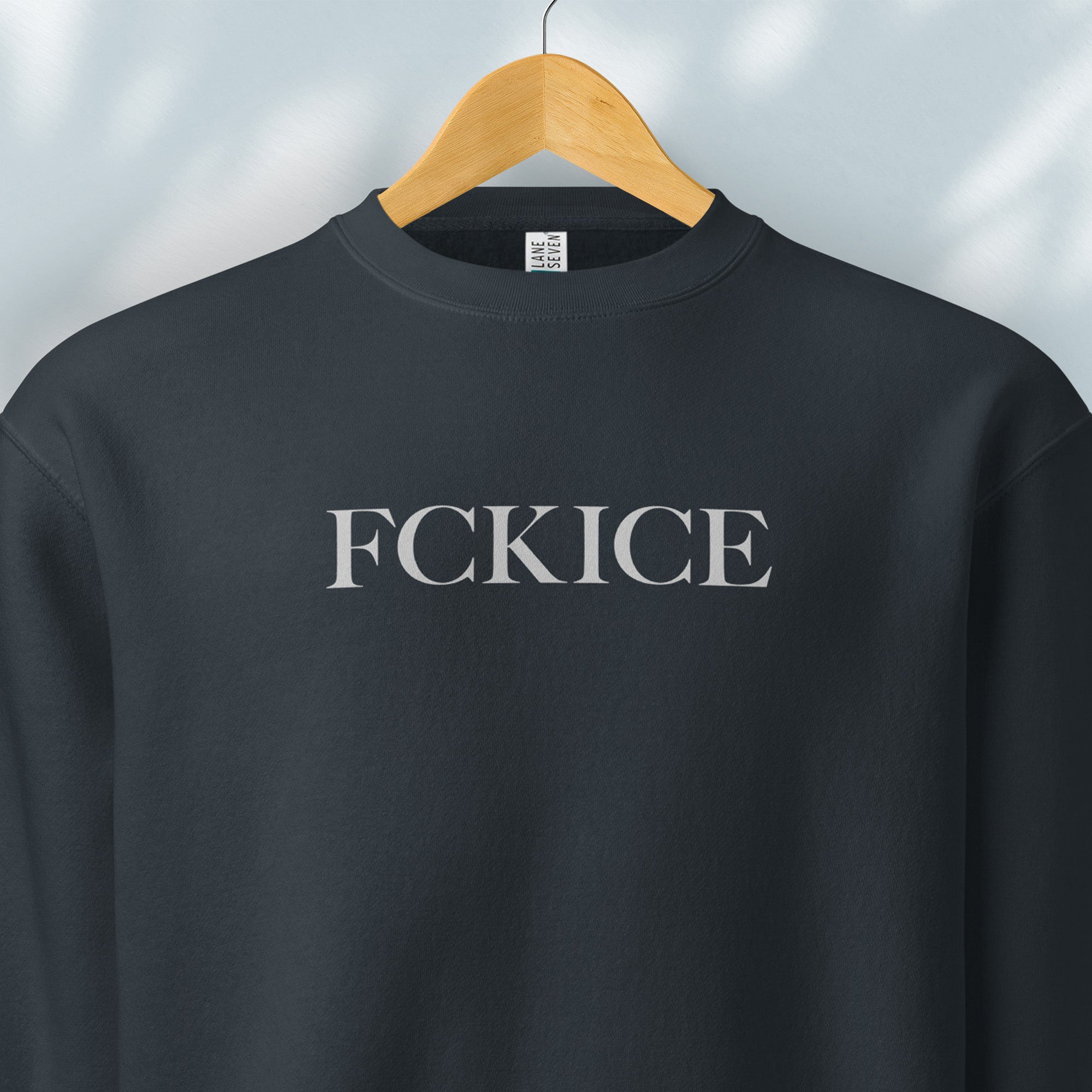 Hanging navy sweatshirt with minimalist serif typography reading “FCK ICE,” an anti-ICE political message opposing Immigration and Customs Enforcement abuses and violence.