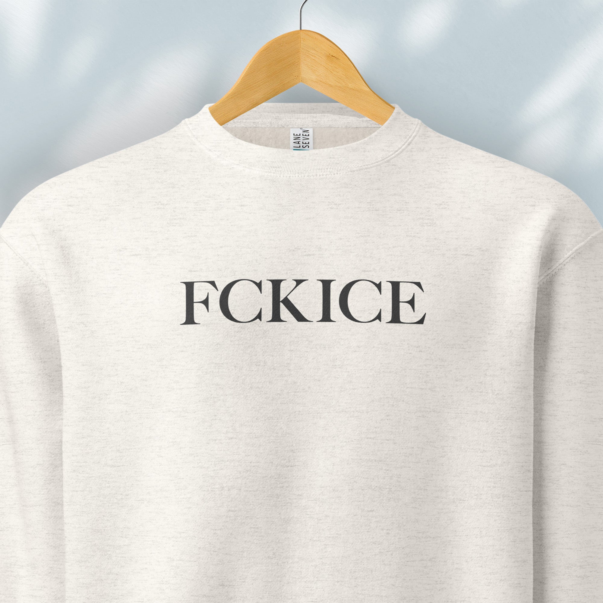 Hanging oatmeal sweatshirt with minimalist serif typography reading “FCK ICE,” an anti-ICE political message opposing Immigration and Customs Enforcement abuses and violence.