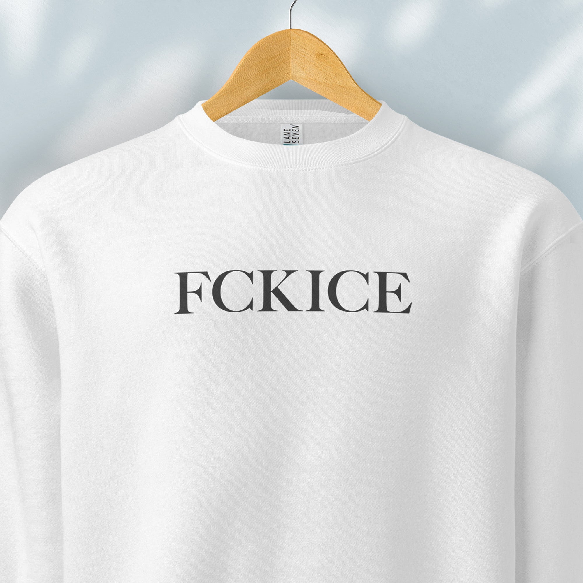 Hanging white sweatshirt with minimalist serif typography reading “FCK ICE,” an anti-ICE political message opposing Immigration and Customs Enforcement abuses and violence.