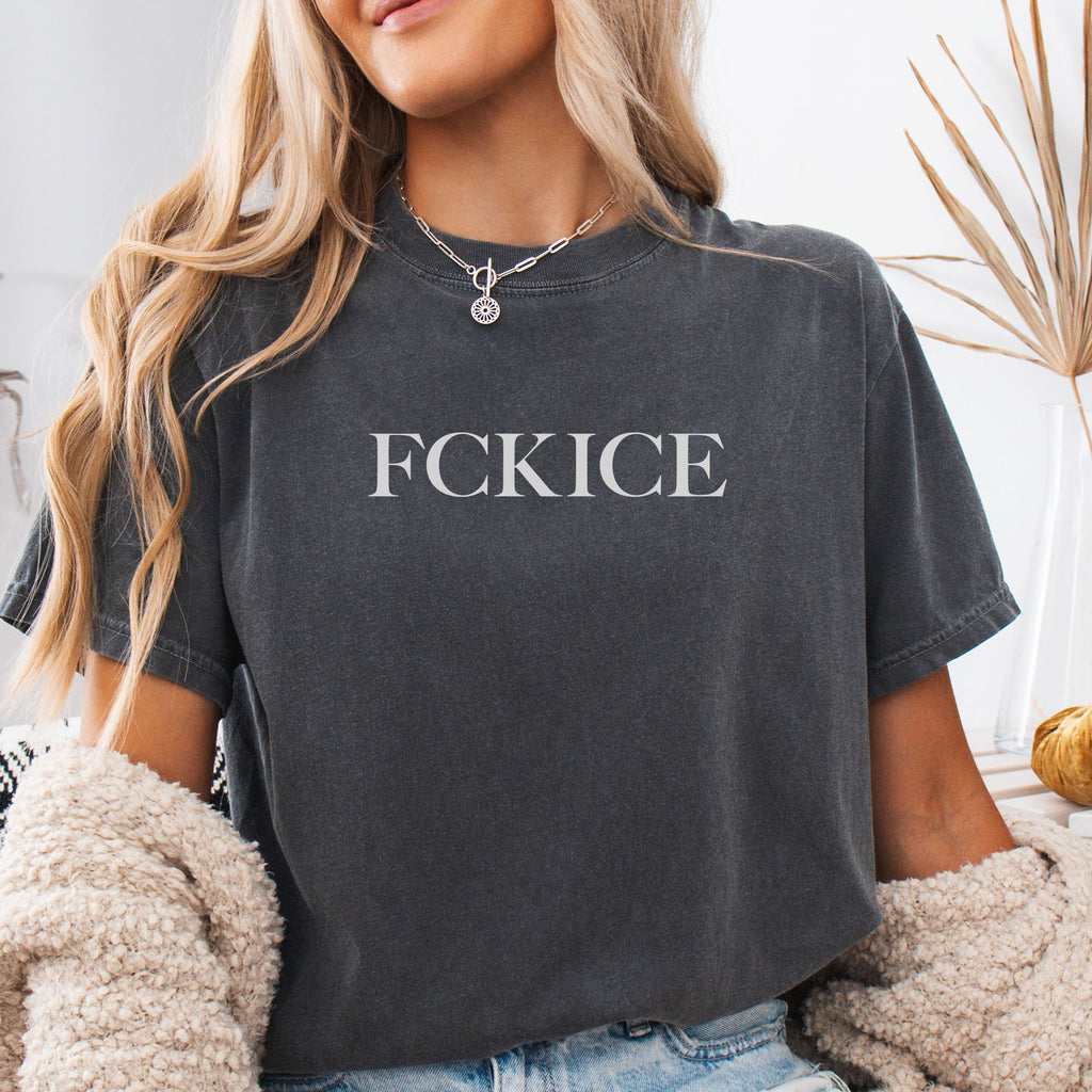 Female model wearing pepper unisex t-shirt with minimalist serif typography reading “FCK ICE,” an anti-ICE, abolish ICE political message opposing Immigration and Customs Enforcement abuses and violence.