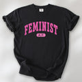 Black Comfort Colors tee with pink text that reads “Feminist A.F.” in a collegiate style.