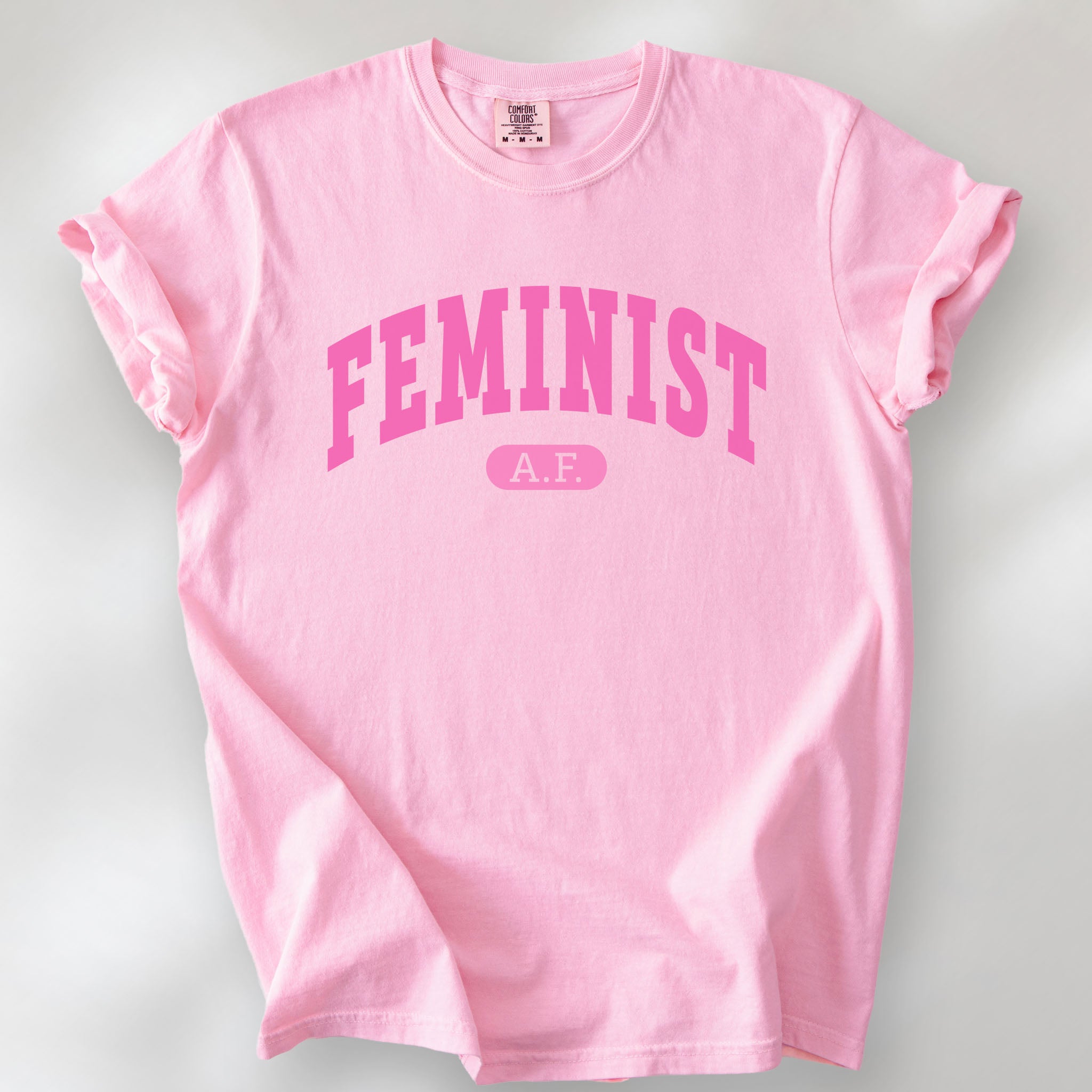 Blossom Comfort Colors tee with pink text that reads “Feminist A.F.” in a collegiate style.