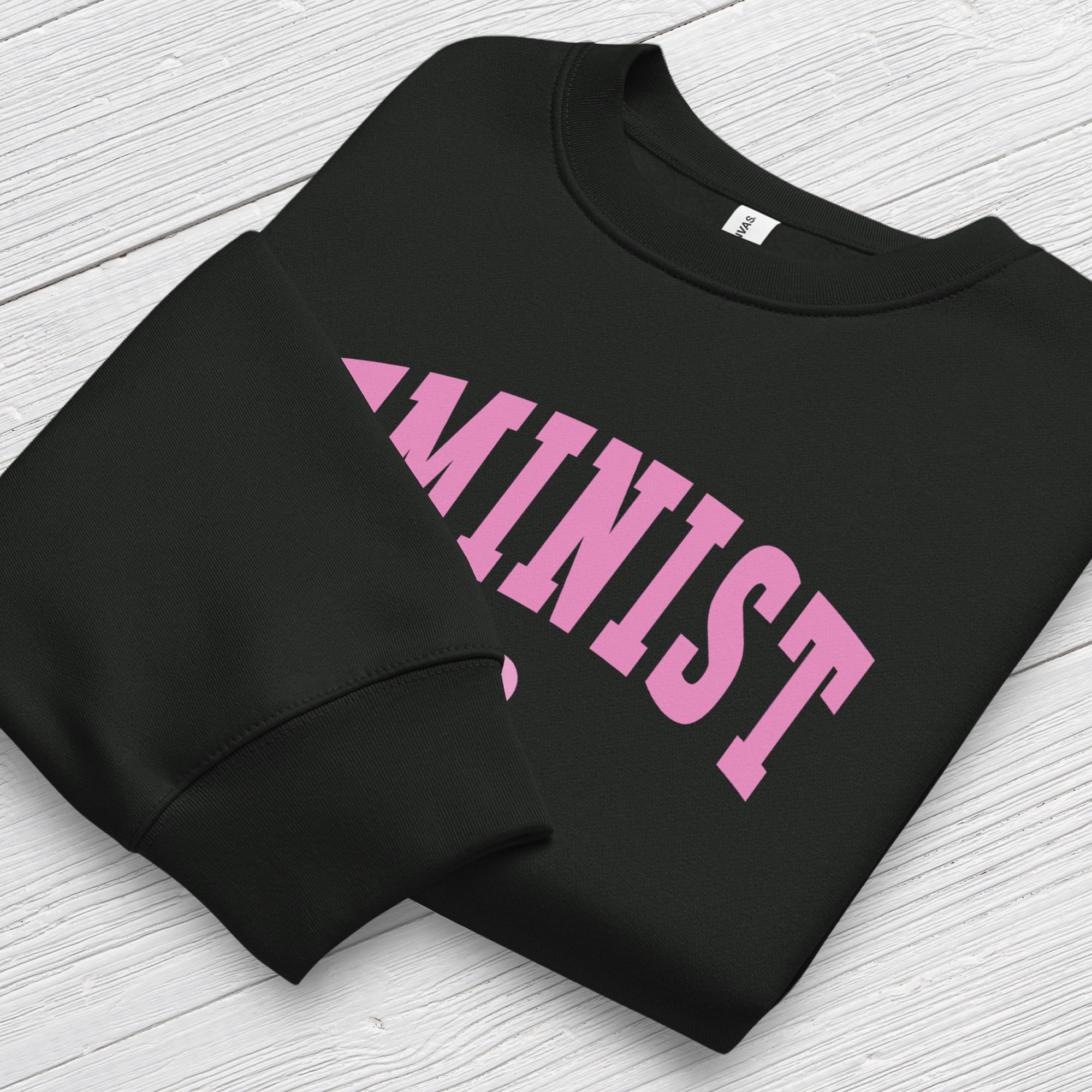 Folded black Bella + Canvas heavyweight sweatshirt with pink text that reads “Feminist A.F.” in a collegiate style, showing closeup of cuffs.