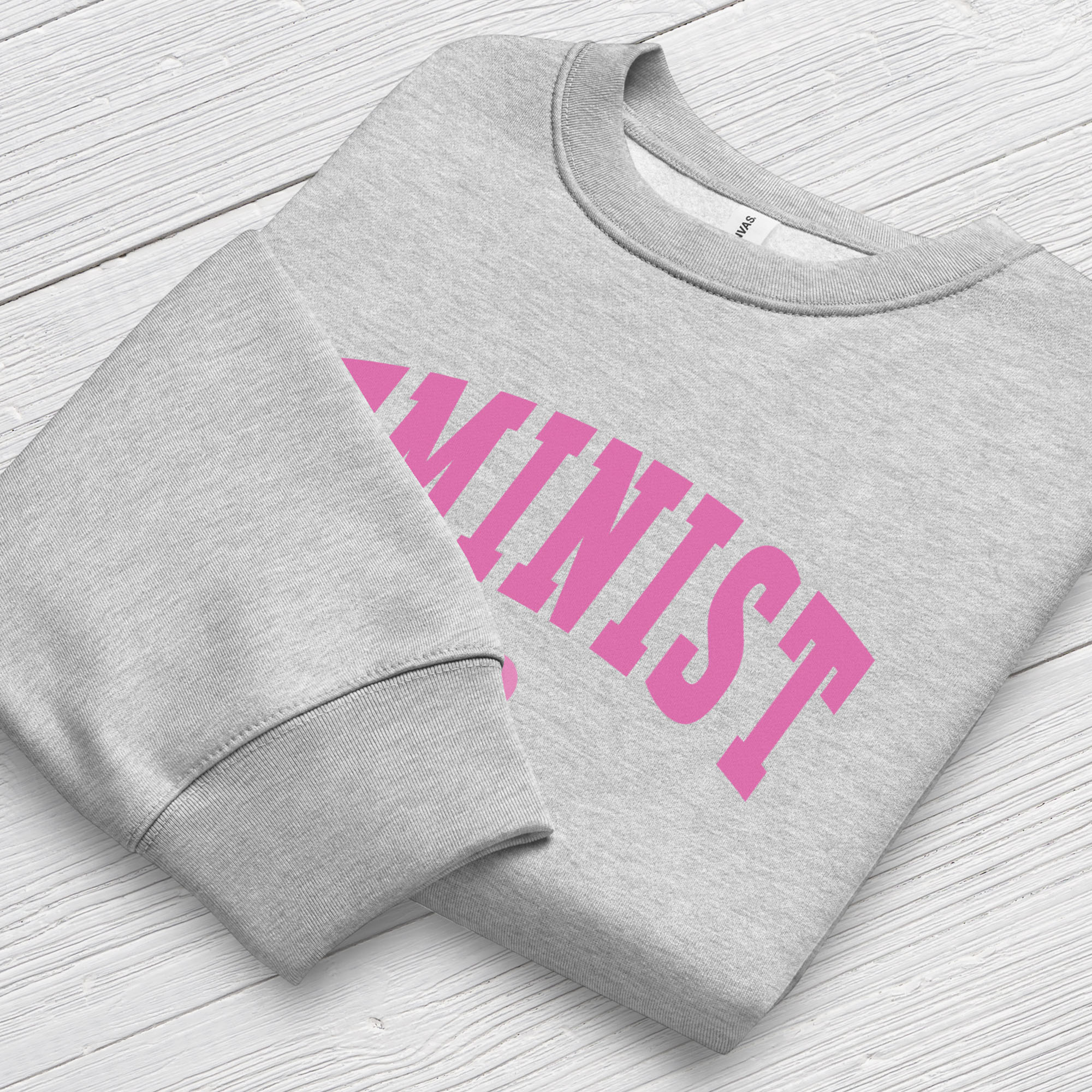 Folded grey Bella + Canvas heavyweight sweatshirt with pink text that reads “Feminist A.F.” in a collegiate style, showing closeup of cuffs.