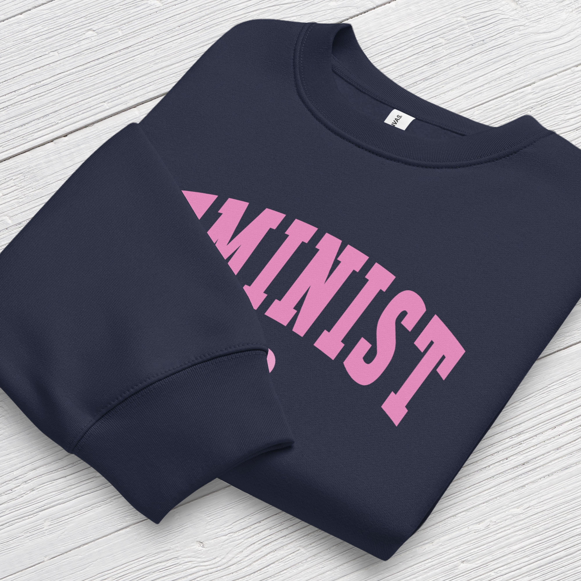 Folded navy Bella + Canvas heavyweight sweatshirt with pink text that reads “Feminist A.F.” in a collegiate style, showing closeup of cuffs.