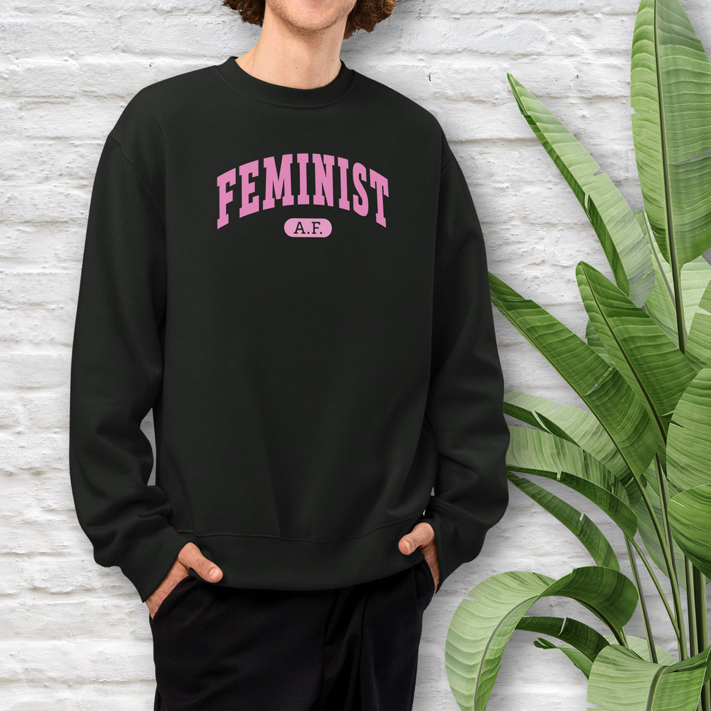Male model wearing black Bella + Canvas heavyweight sweatshirt with pink text that reads “Feminist A.F.” in a collegiate style.