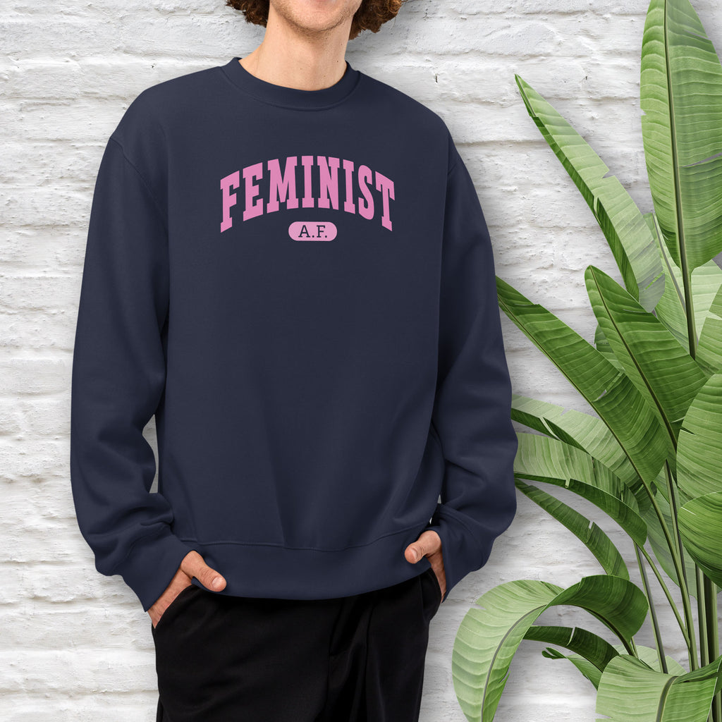 Male model wearing navy Bella + Canvas heavyweight sweatshirt with pink text that reads “Feminist A.F.” in a collegiate style.
