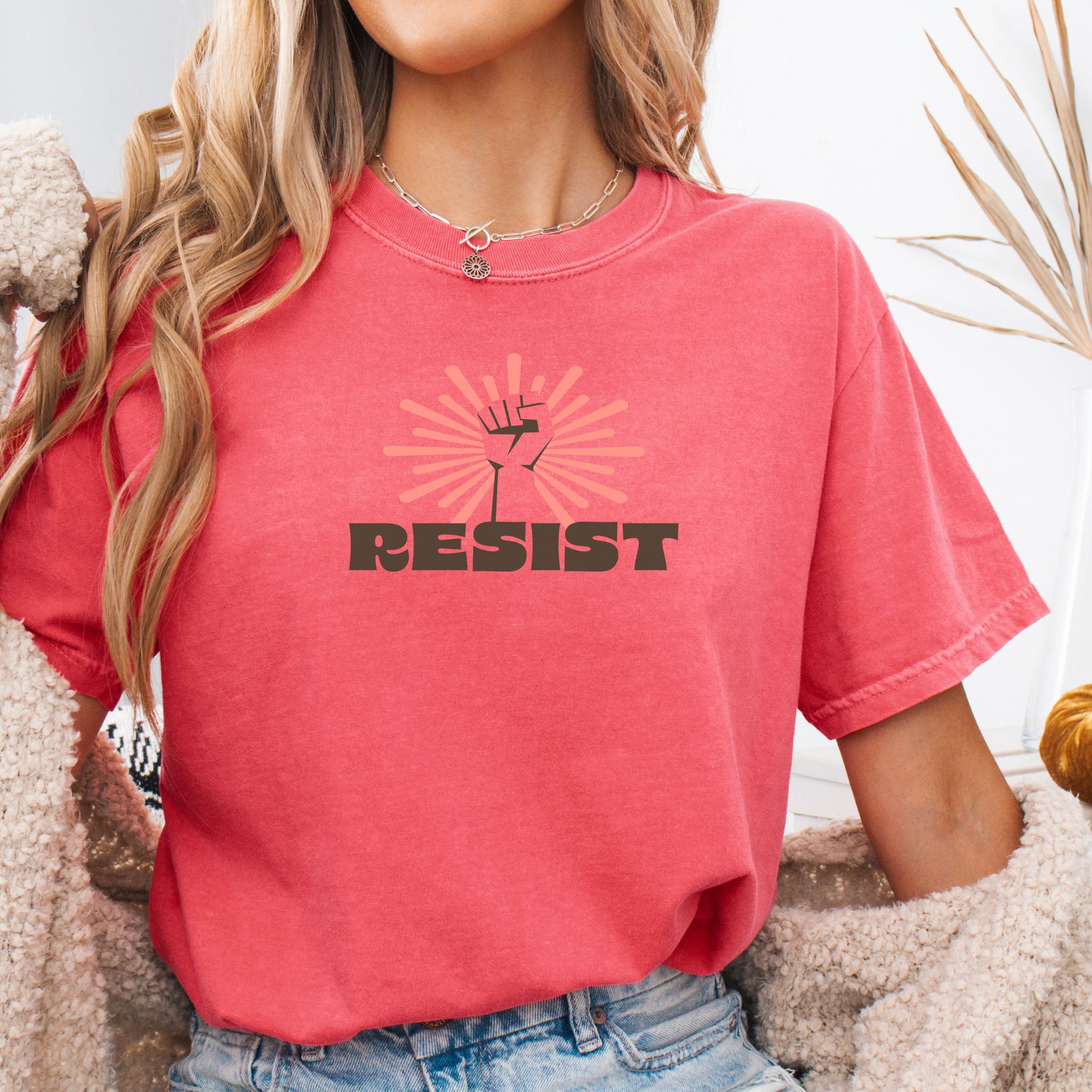 Person wearing a watermelon red colored t-shirt with 'RESIST' graphic design.