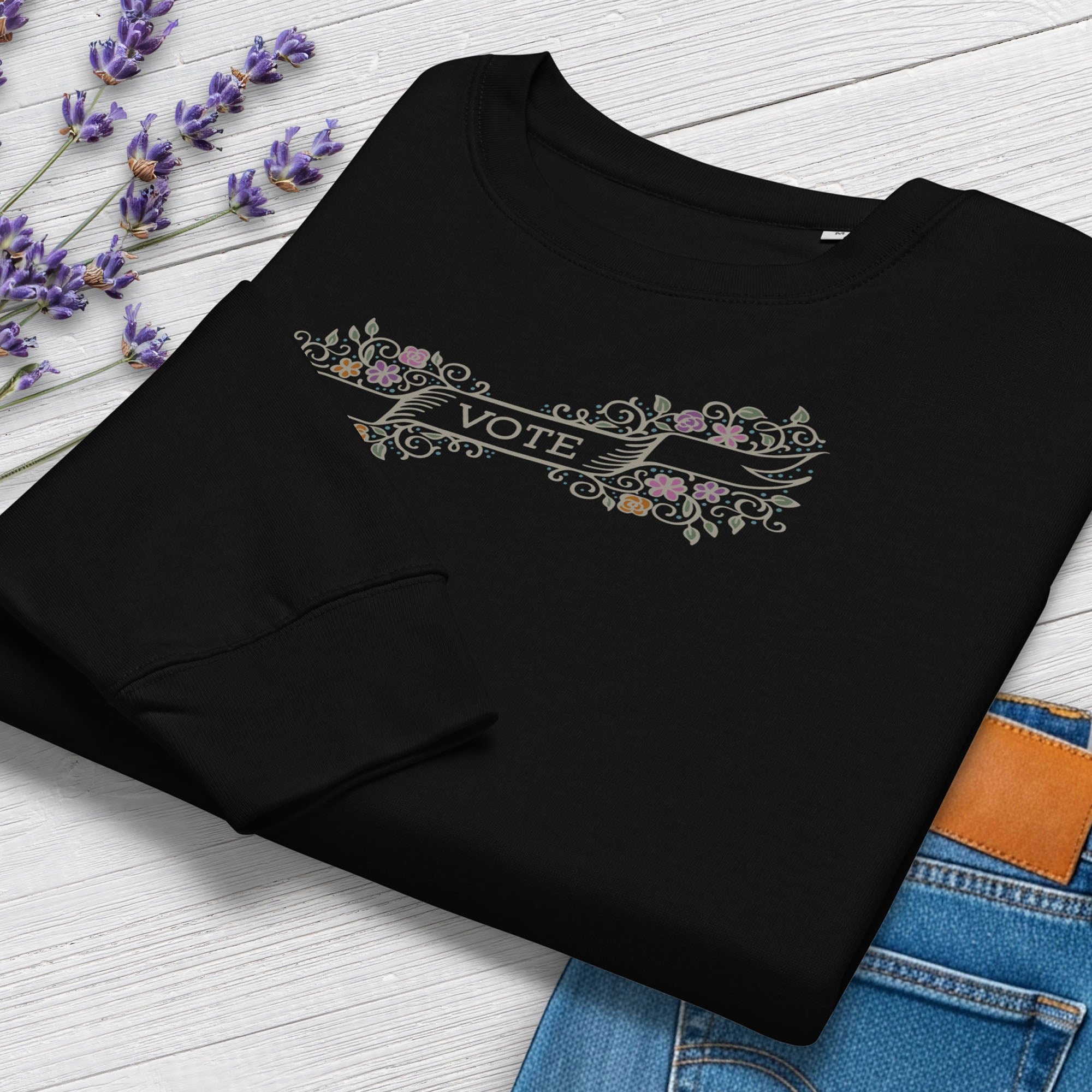 Folded women's black sweatshirt with vintage style floral illustration and a banner reading “vote” in the center, showing cuff and closeup detail.