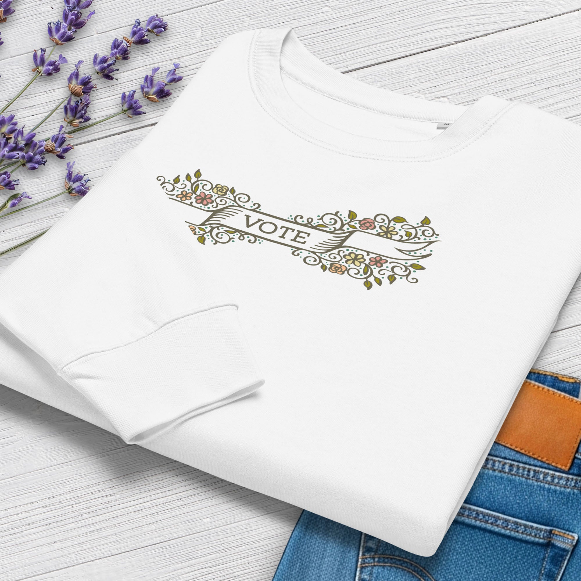 Folded women's white sweatshirt with vintage style floral illustration and a banner reading “vote” in the center, showing cuff and closeup detail.