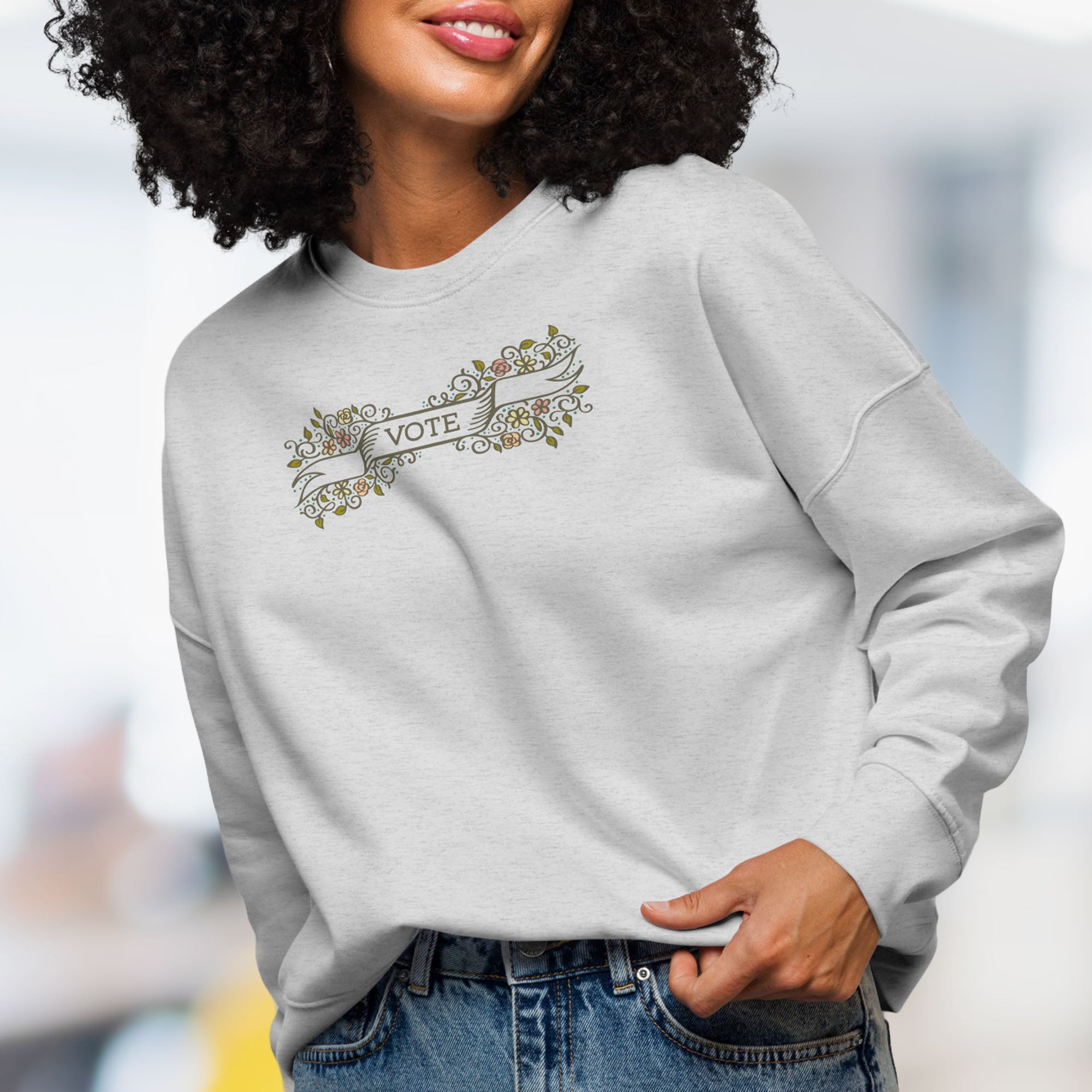 Female model wearing women's grey sweatshirt with vintage style floral illustration and a banner reading “vote” in the center.