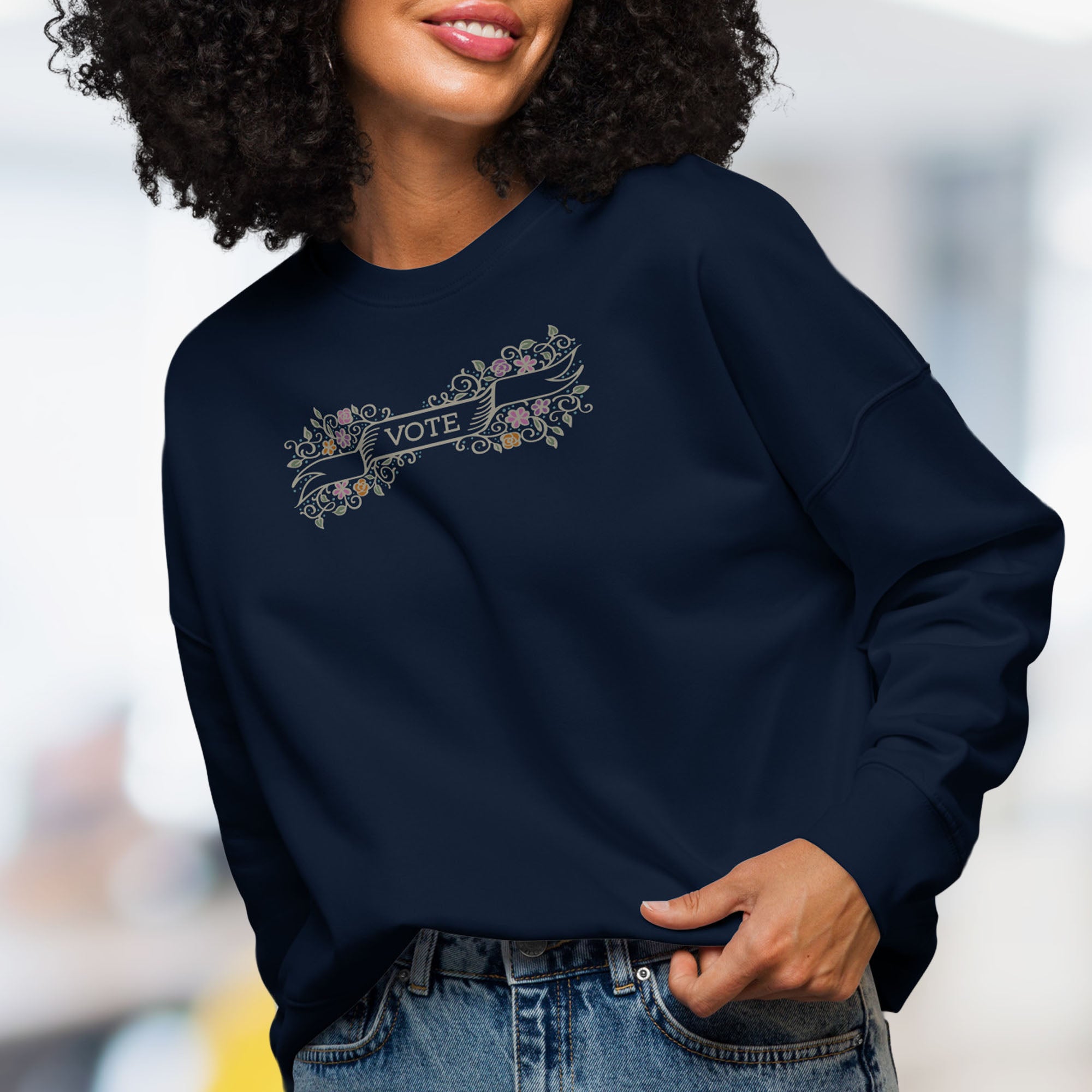 Female model wearing women's navy sweatshirt with vintage style floral illustration and a banner reading “vote” in the center.
