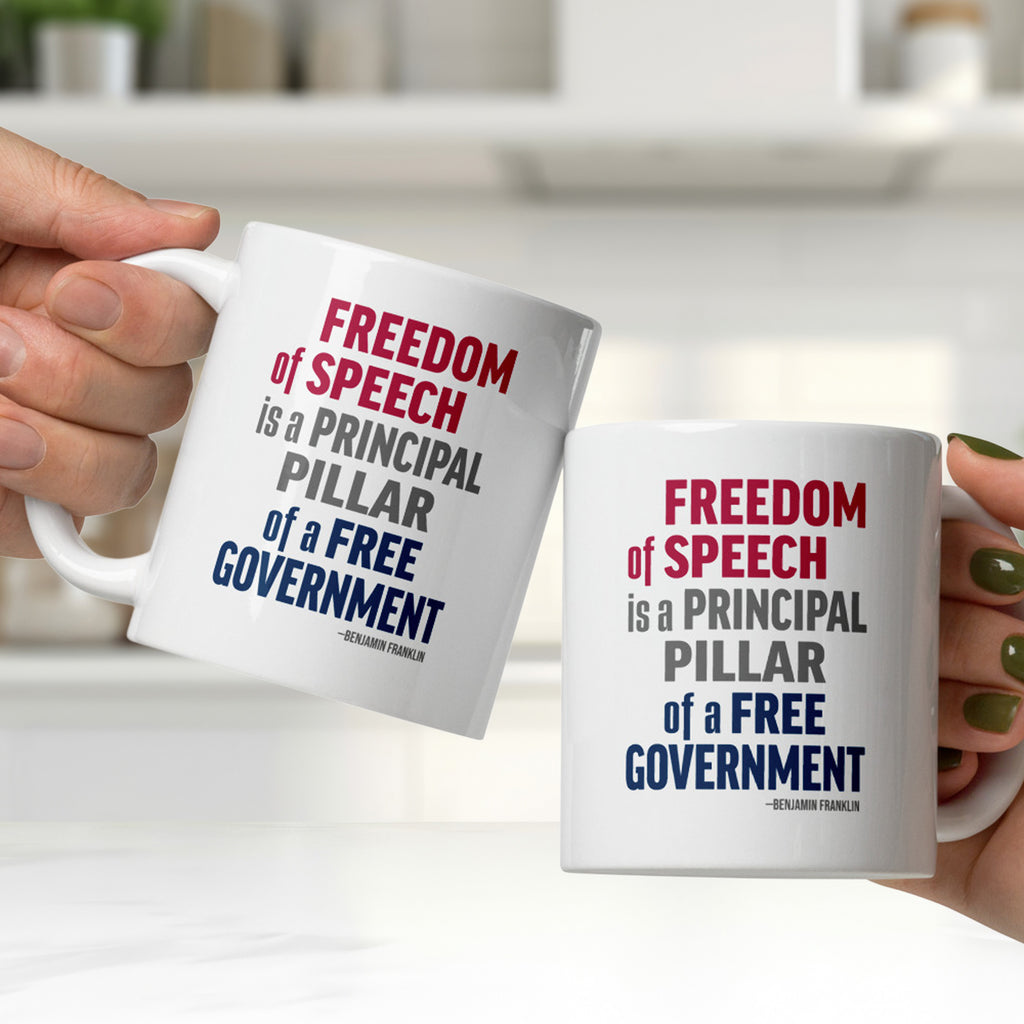 Two people clinking white ceramic mugs in a kitchen, with mugs that have with bold patriotic red, blue, and grey text that reads "Freedom of speech is a principal pillar of a free government. – Ben Franklin."