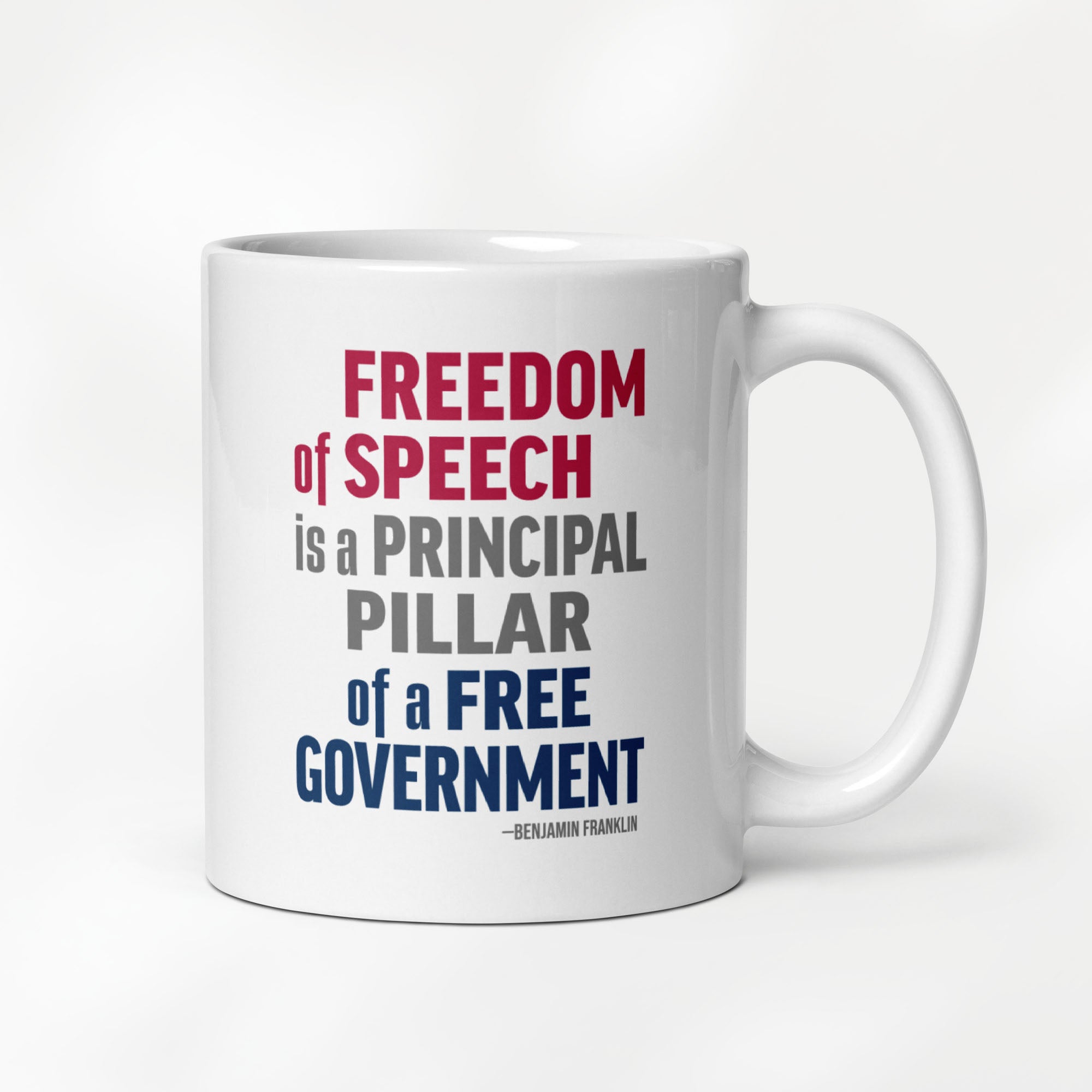 11 ounce white ceramic mug with bold patriotic red, blue, and grey text that reads "Freedom of speech is a principal pillar of a free government. – Ben Franklin." 