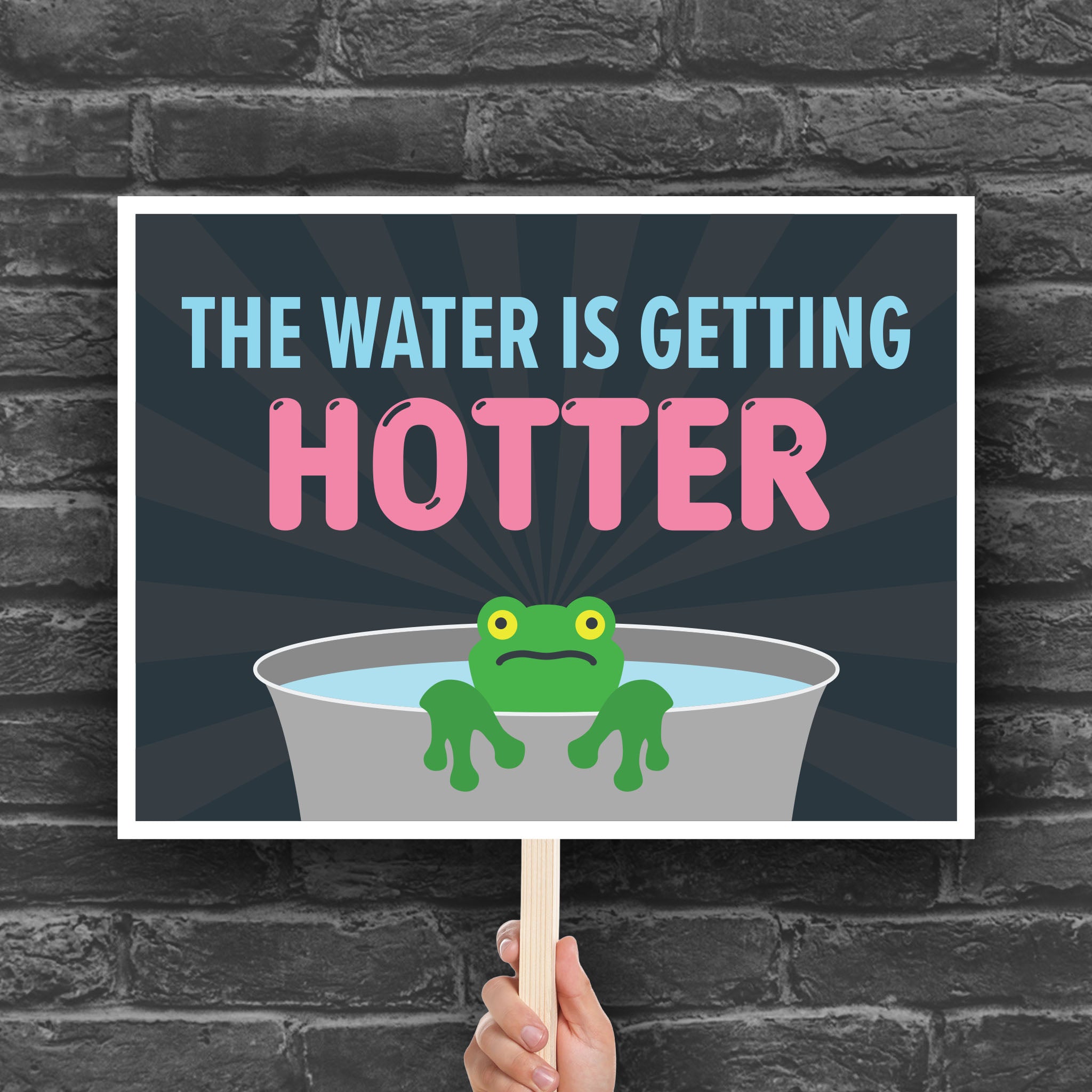 Downloadable, printable anti-trump protest sign with bold text in blue and pink that says "The water is getting hotter" above a cartoon illustration of a panicked frog in a pot of water.