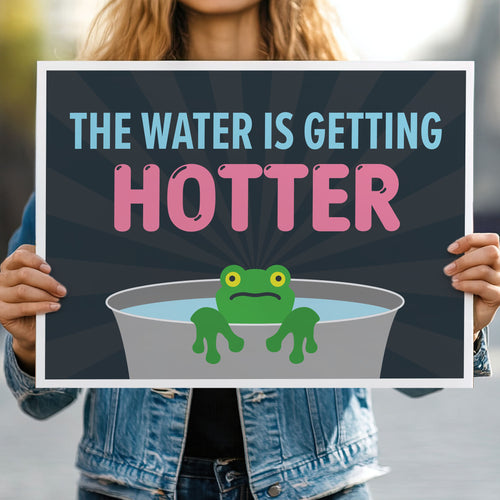 Person holding anti-trump protest sign with bold text in blue and pink that says "The water is getting hotter" above a cartoon illustration of a panicked frog in a pot of water.