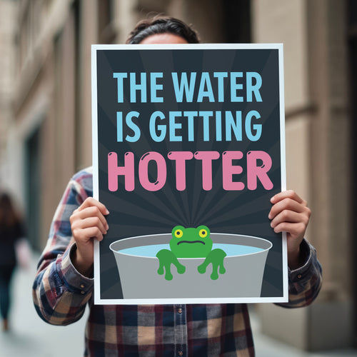 Person holding anti-trump protest sign with bold text in blue and pink that says "The water is getting hotter" above a cartoon illustration of a panicked frog in a pot of water.