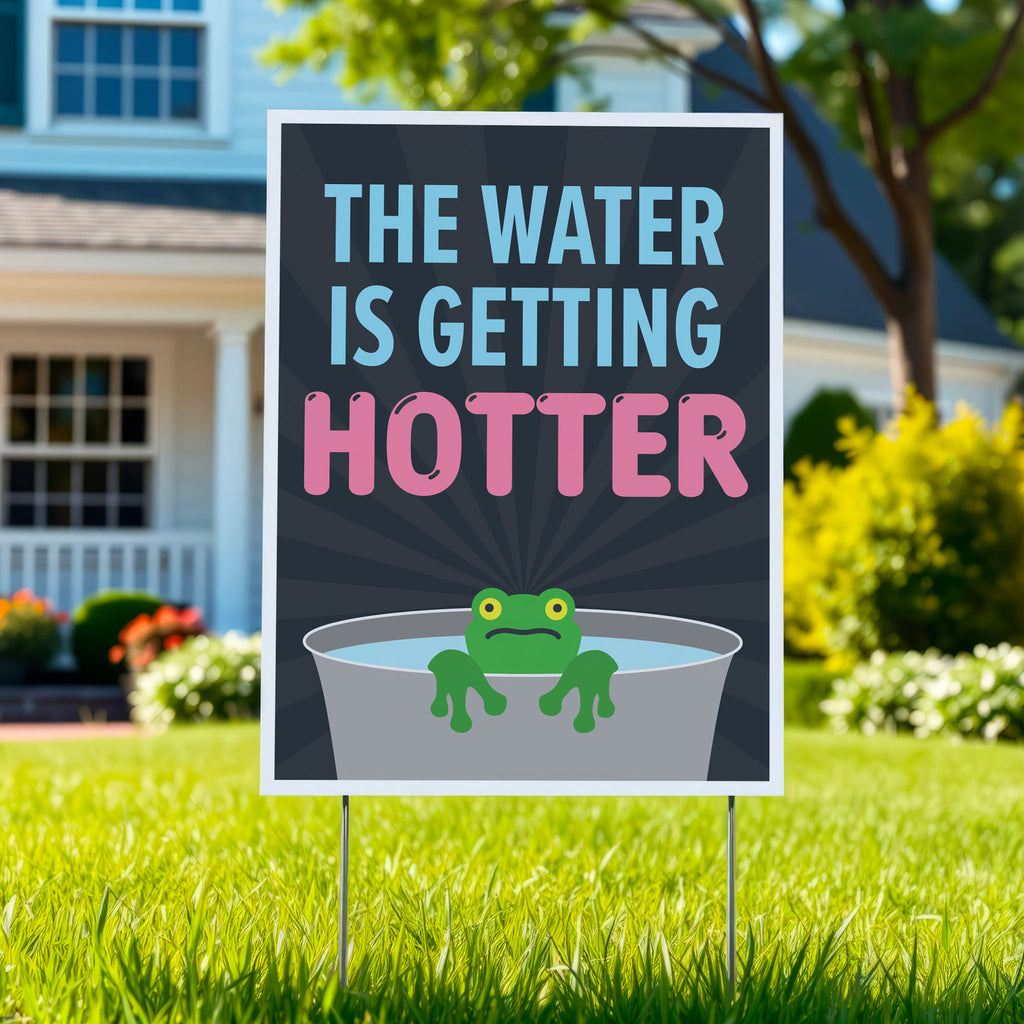 Anti-trump yard sign with bold text in blue and pink that says "The water is getting hotter" above a cartoon illustration of a panicked frog in a pot of water, planted in a green lawn.
