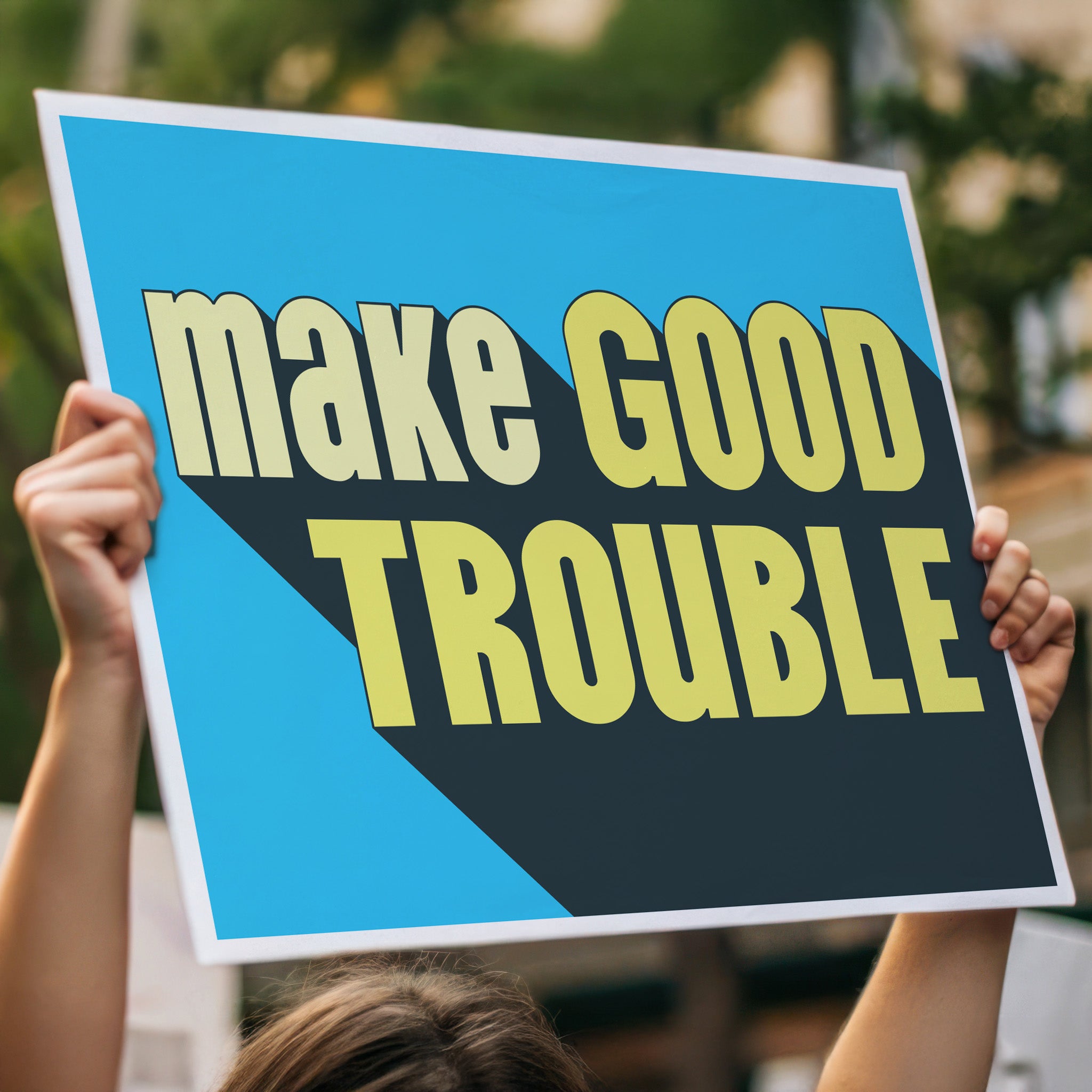 Person holding high above a crowd, a protest sign with bold text reading "Make Good Trouble" – a tribute to John Lewis’ legacy and a call for courageous, principled resistance against injustice.
