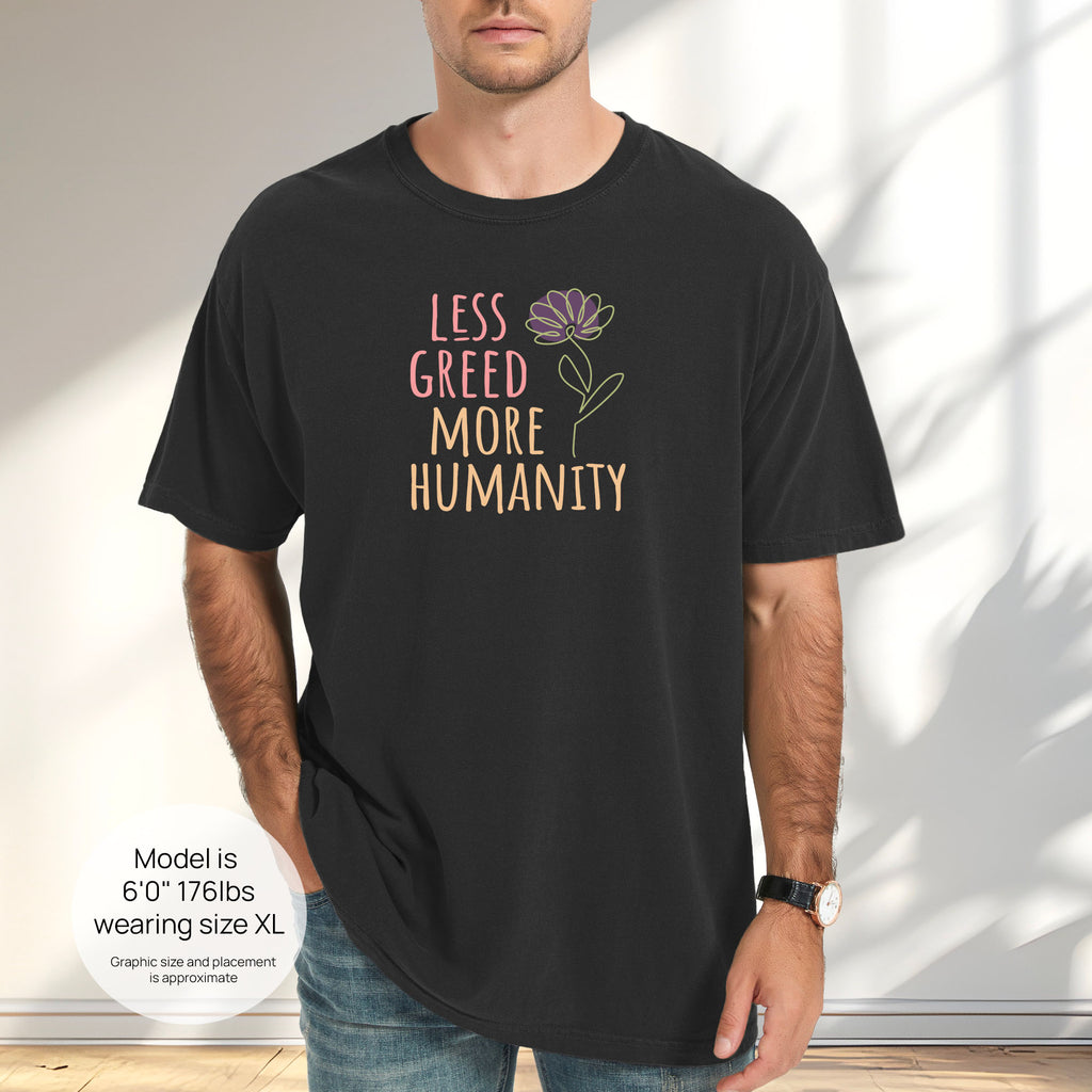 Male model wearing black t-shirt featuring the phrase “Less Greed More Humanity” in friendly typography with a simple yellow flower illustration. Includes size and fit information for the model who is 6 feet 0 inches, 176 pounds, and wearing a size XL shirt.
