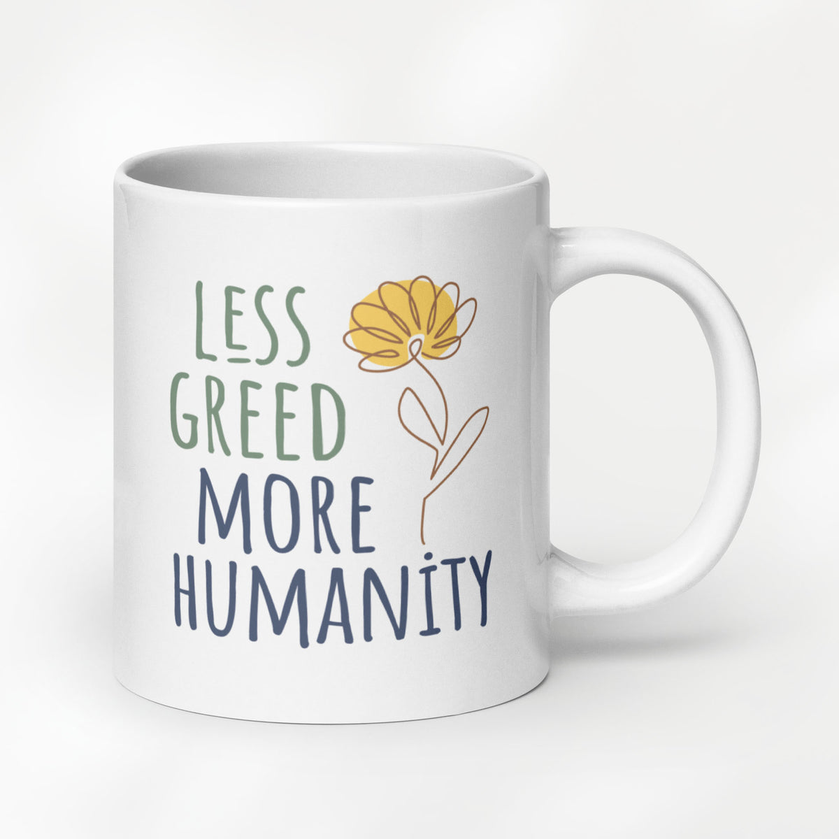 20 ounce white ceramic mug featuring the phrase “Less Greed More Humanity” in hand-lettered typography with green and blue text alongside a simple yellow flower illustration.