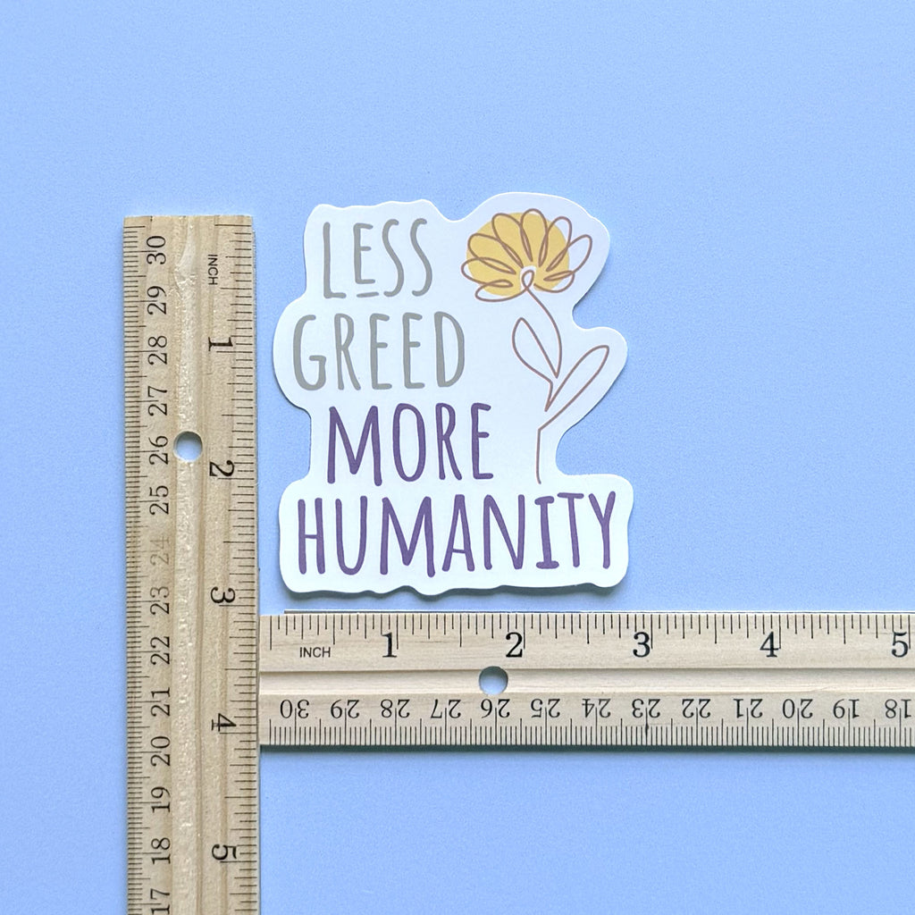 Less Greed More Humanity matte vinyl die-cut sticker with a minimalist yellow flower illustration, with two rulers showing the approximate sticker size of 3 inches by 3 inches.