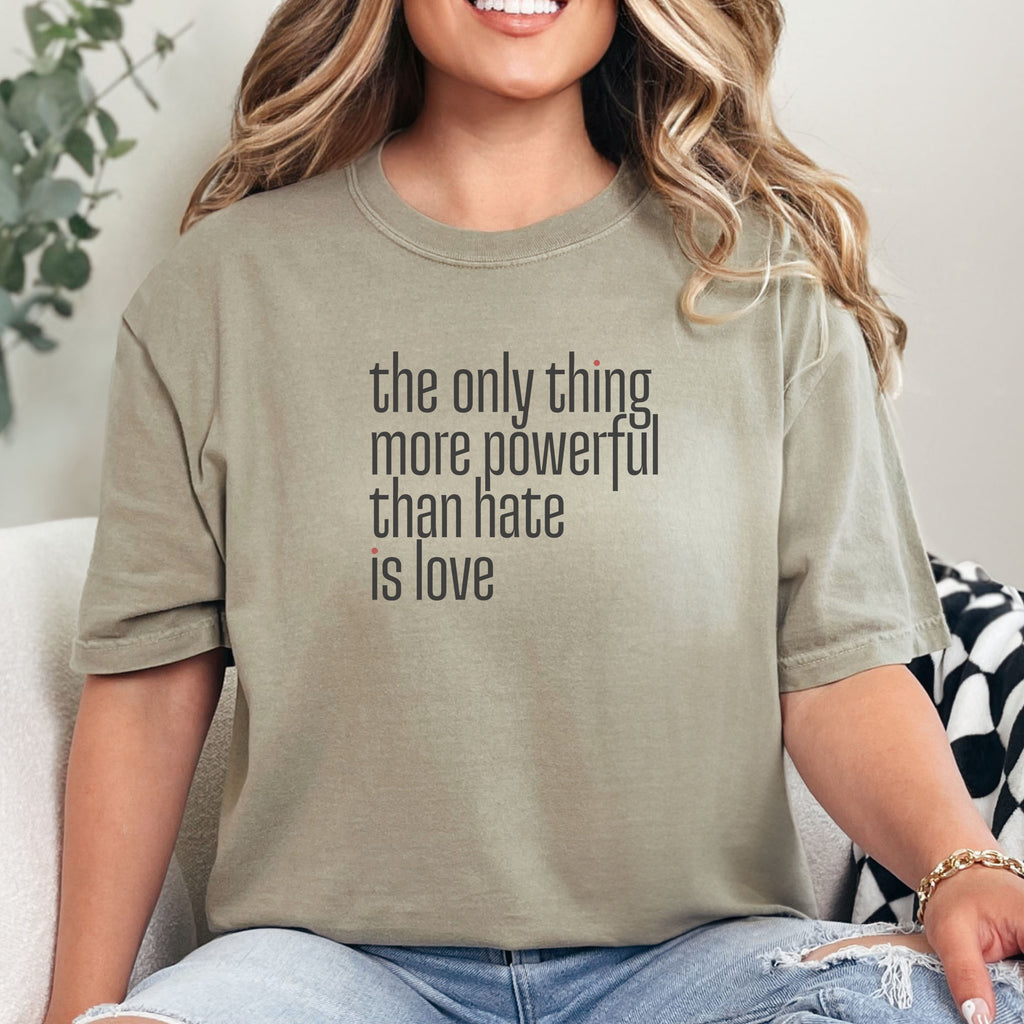 Female model wearing khaki t-shirt with a stylized text block reading “the only thing more powerful than hate is love."