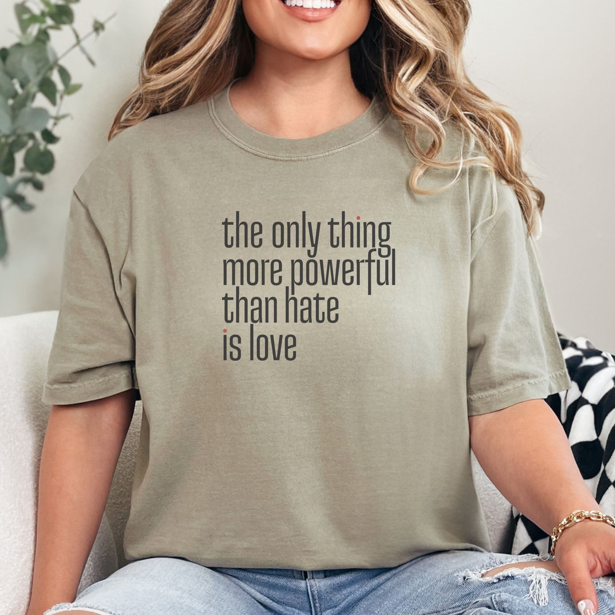 Female model wearing khaki t-shirt with a stylized text block reading “the only thing more powerful than hate is love."