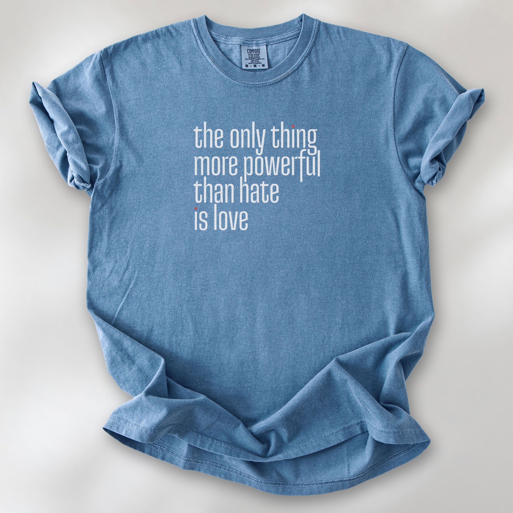 Blue jean t-shirt with a stylized text block reading “the only thing more powerful than hate is love." 
