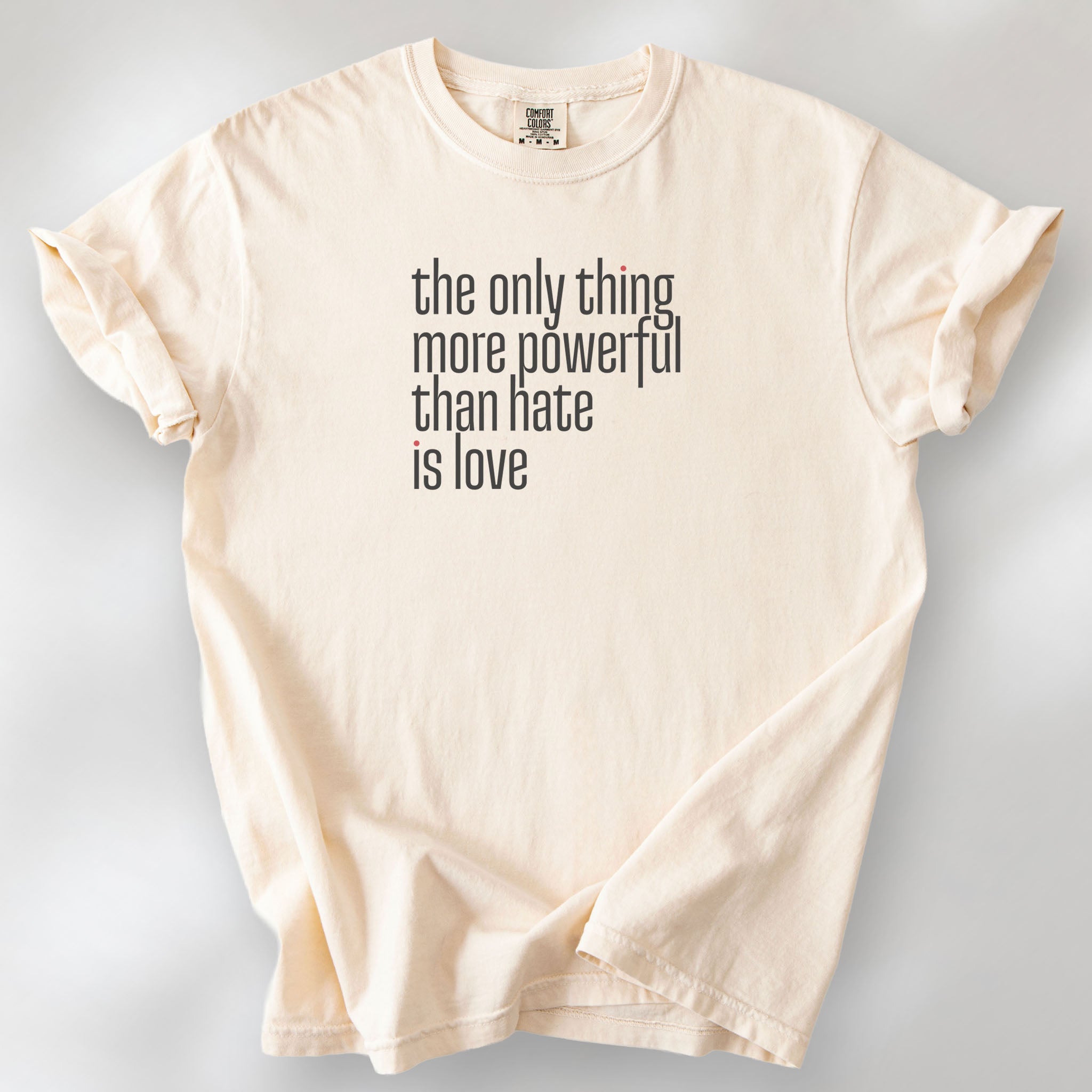 Ivory t-shirt with a stylized text block reading “the only thing more powerful than hate is love."