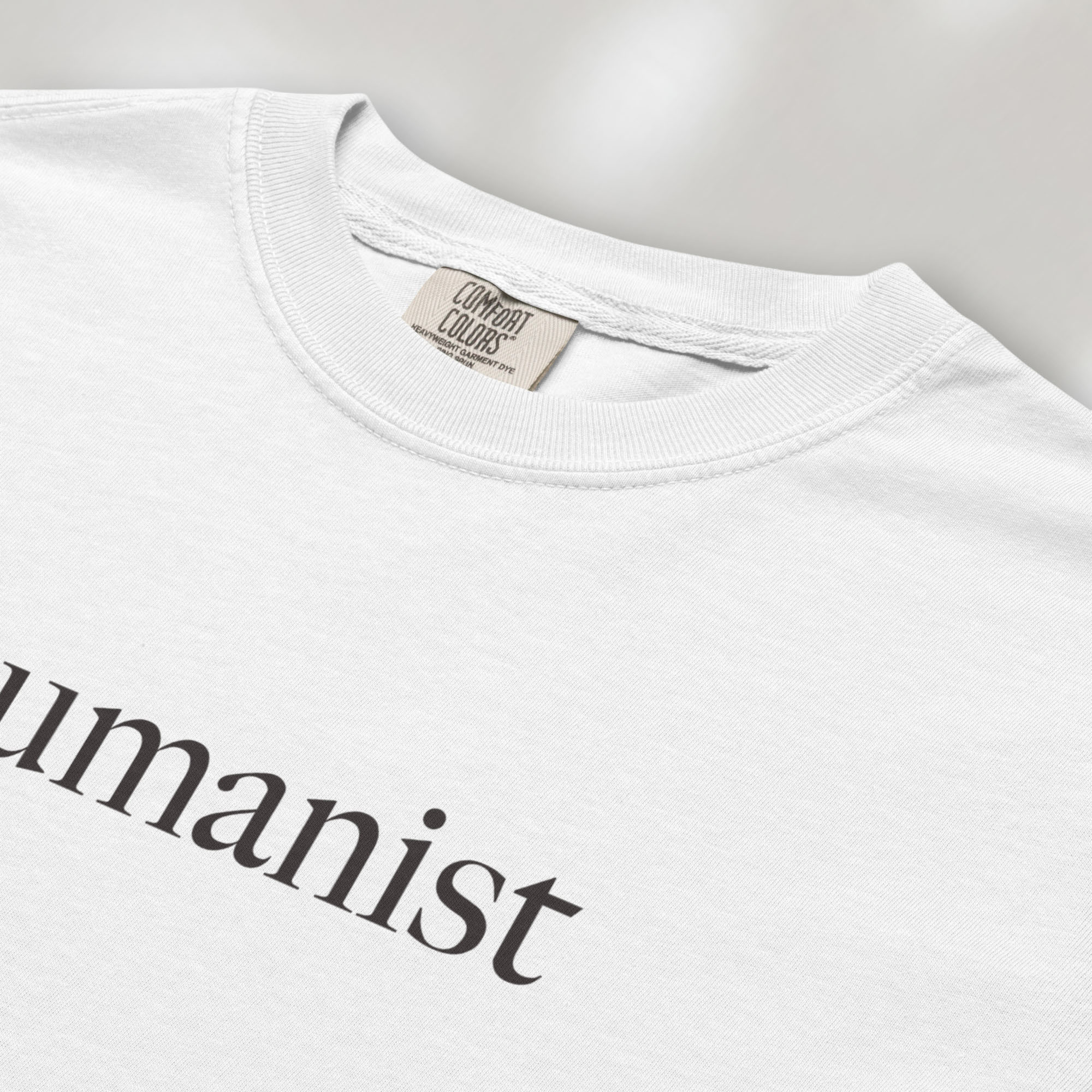 Closeup detail of white Comfort Colors t-shirt with minimalist serif text reading “humanist”.