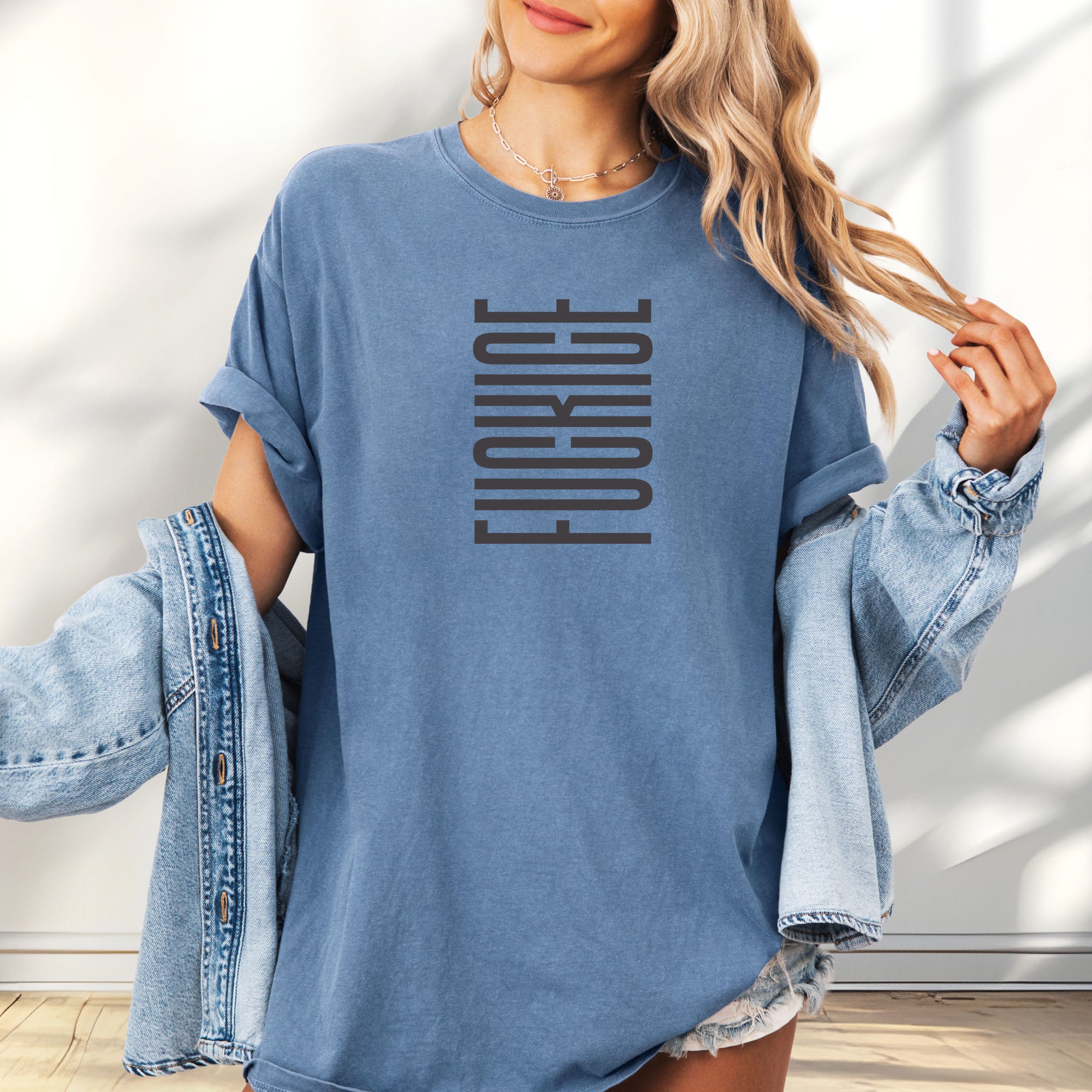 Female model wearing oversized blue jean t-shirt with minimalist geometric design that subtly spells “Fuck ICE” using stacked bars and negative space, hidden protest message shirt.