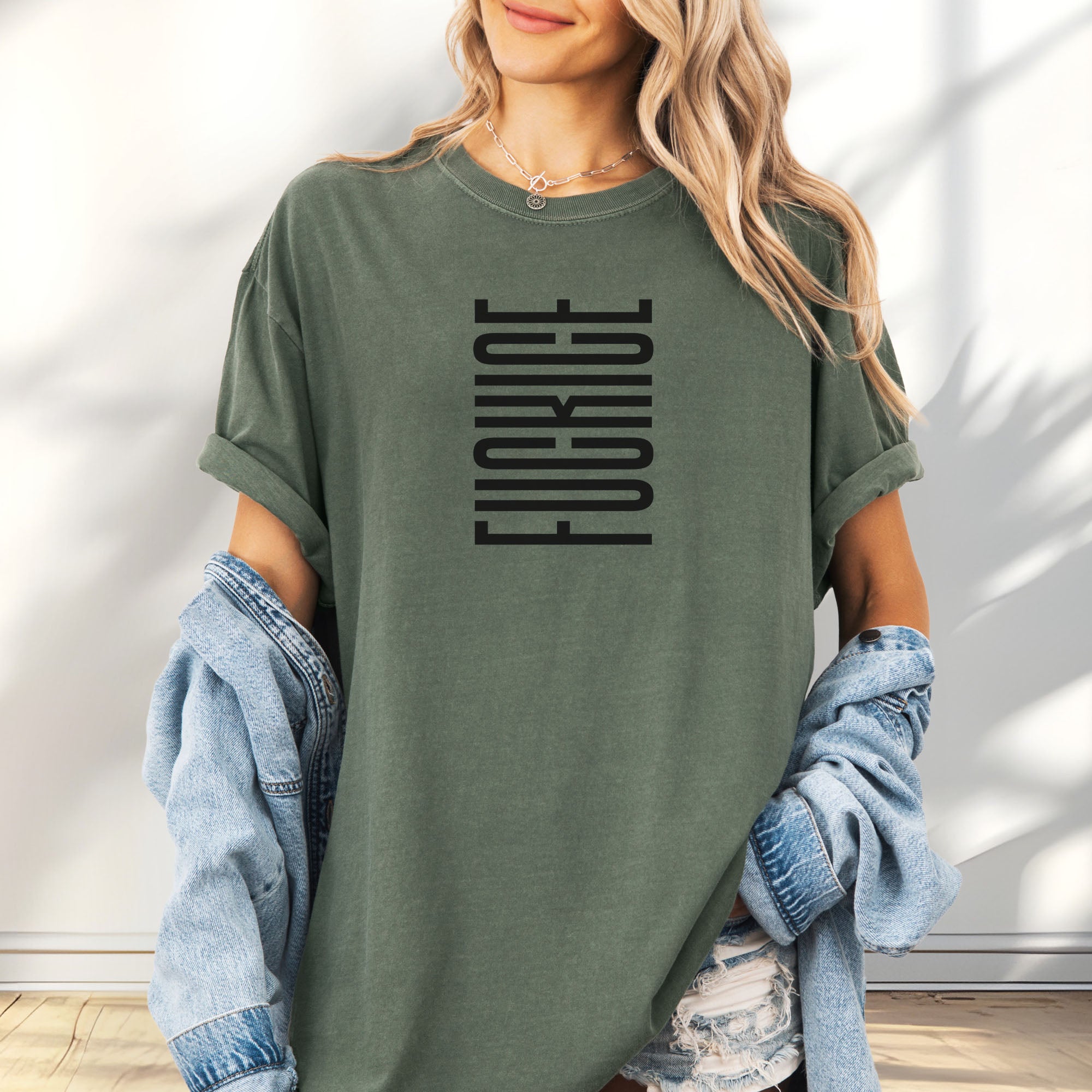 Female model wearing oversized moss t-shirt with minimalist black geometric design that subtly spells “Fuck ICE” using stacked bars and negative space, hidden protest message shirt.