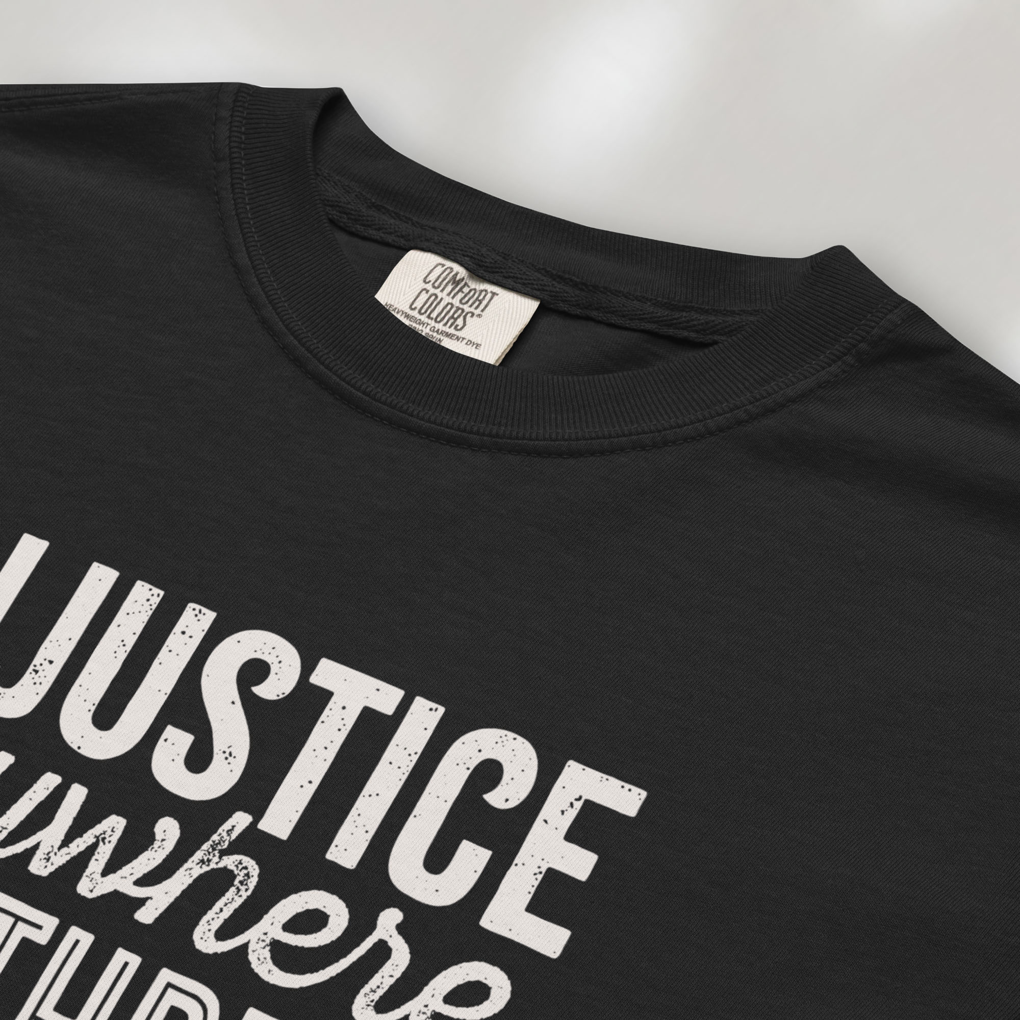 Closeup detail of black t-shirt with bold text reading “Injustice anywhere is a threat to justice everywhere” quote from Martin Luther King Jr, MLK Jr, Letter from Birmingham jail — civil rights protest apparel for activists.