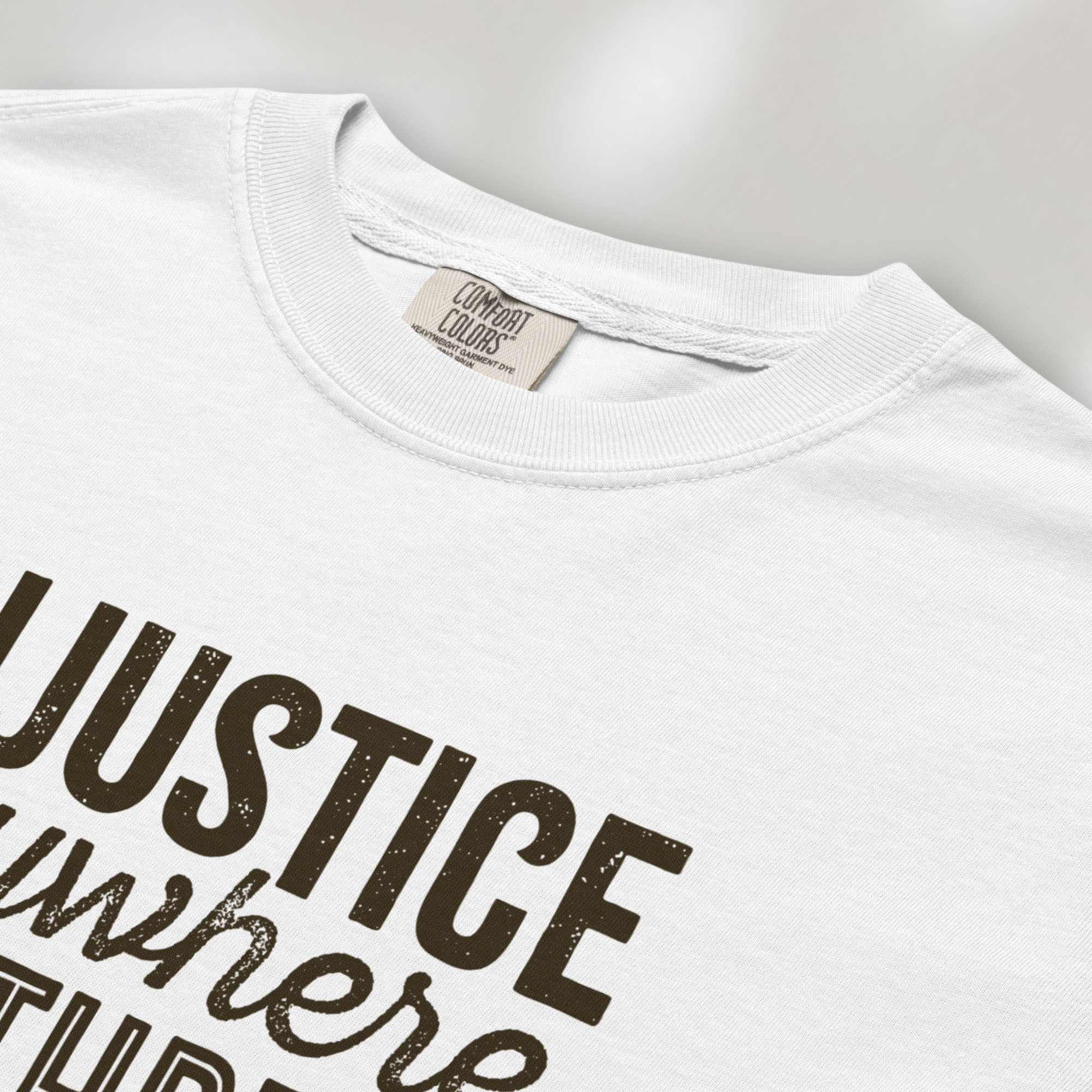 Closeup detail of white t-shirt with bold text reading “Injustice anywhere is a threat to justice everywhere” quote from Martin Luther King Jr, MLK Jr, Letter from Birmingham jail — civil rights protest apparel for activists.