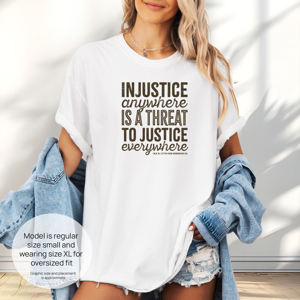 Female model wearing white t-shirt with bold text reading “Injustice anywhere is a threat to justice everywhere” quote from Martin Luther King Jr, MLK Jr, Letter from Birmingham jail — civil rights protest apparel for activists. Includes size and fit information for the model who is regular size small, and wearing a size XL shirt for an oversized fit.
