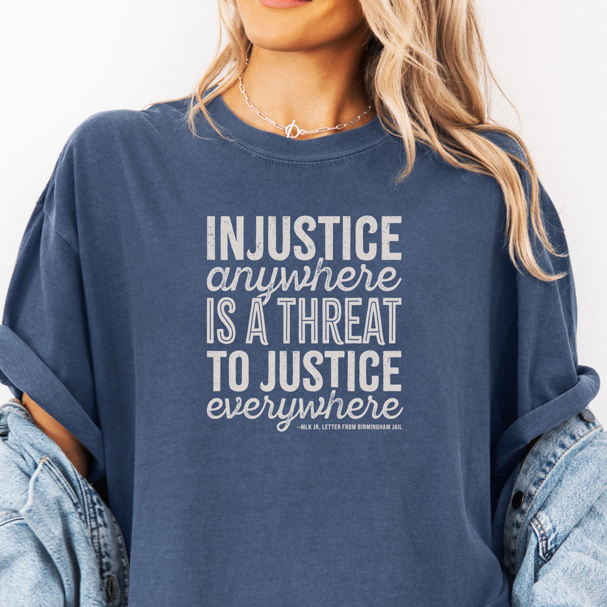 Female model wearing oversized denim t-shirt with bold text reading “Injustice anywhere is a threat to justice everywhere” quote from Martin Luther King Jr, MLK Jr, Letter from Birmingham jail — civil rights protest apparel for activists.