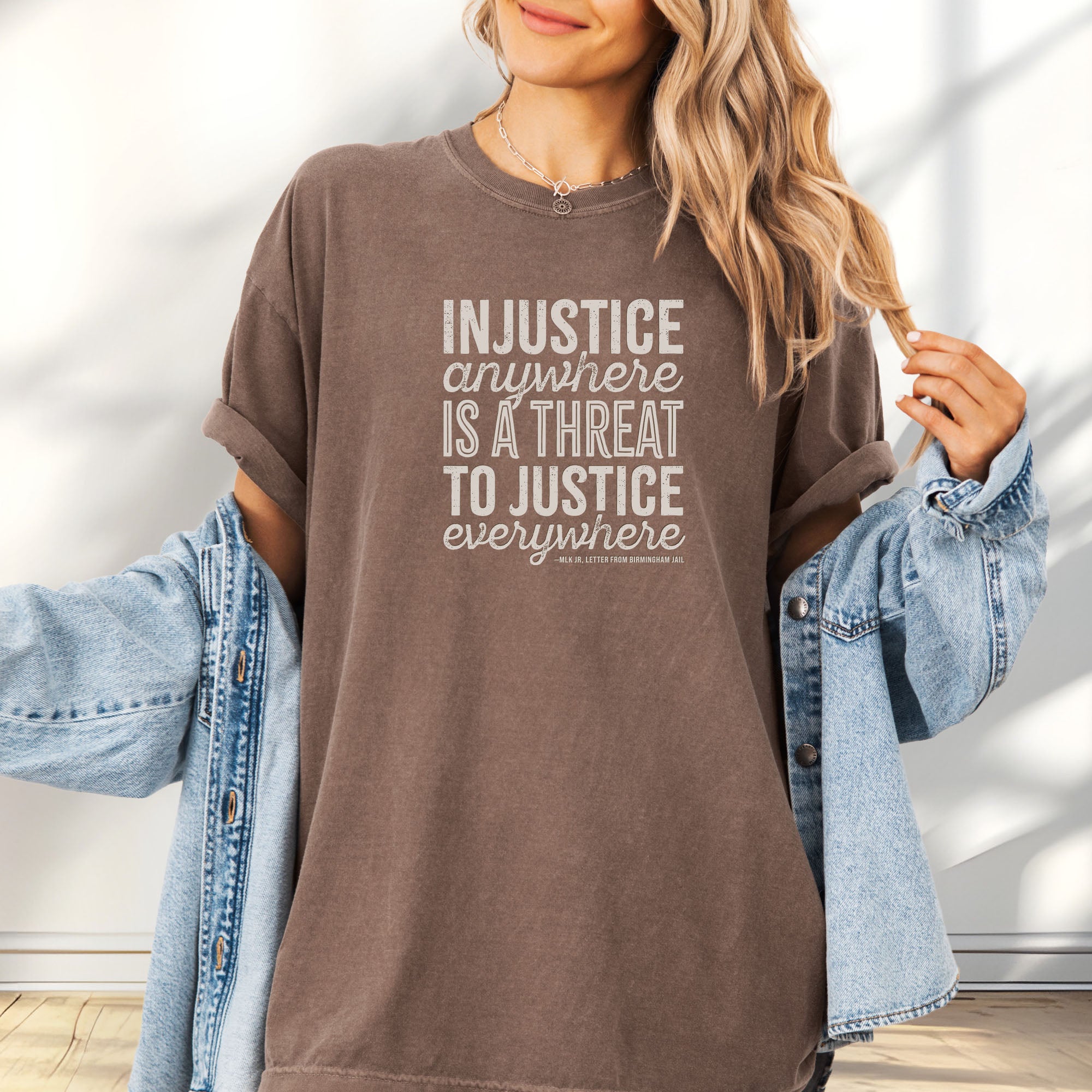 Female model wearing oversized espresso t-shirt with bold text reading “Injustice anywhere is a threat to justice everywhere” quote from Martin Luther King Jr, MLK Jr, Letter from Birmingham jail — civil rights protest apparel for activists.