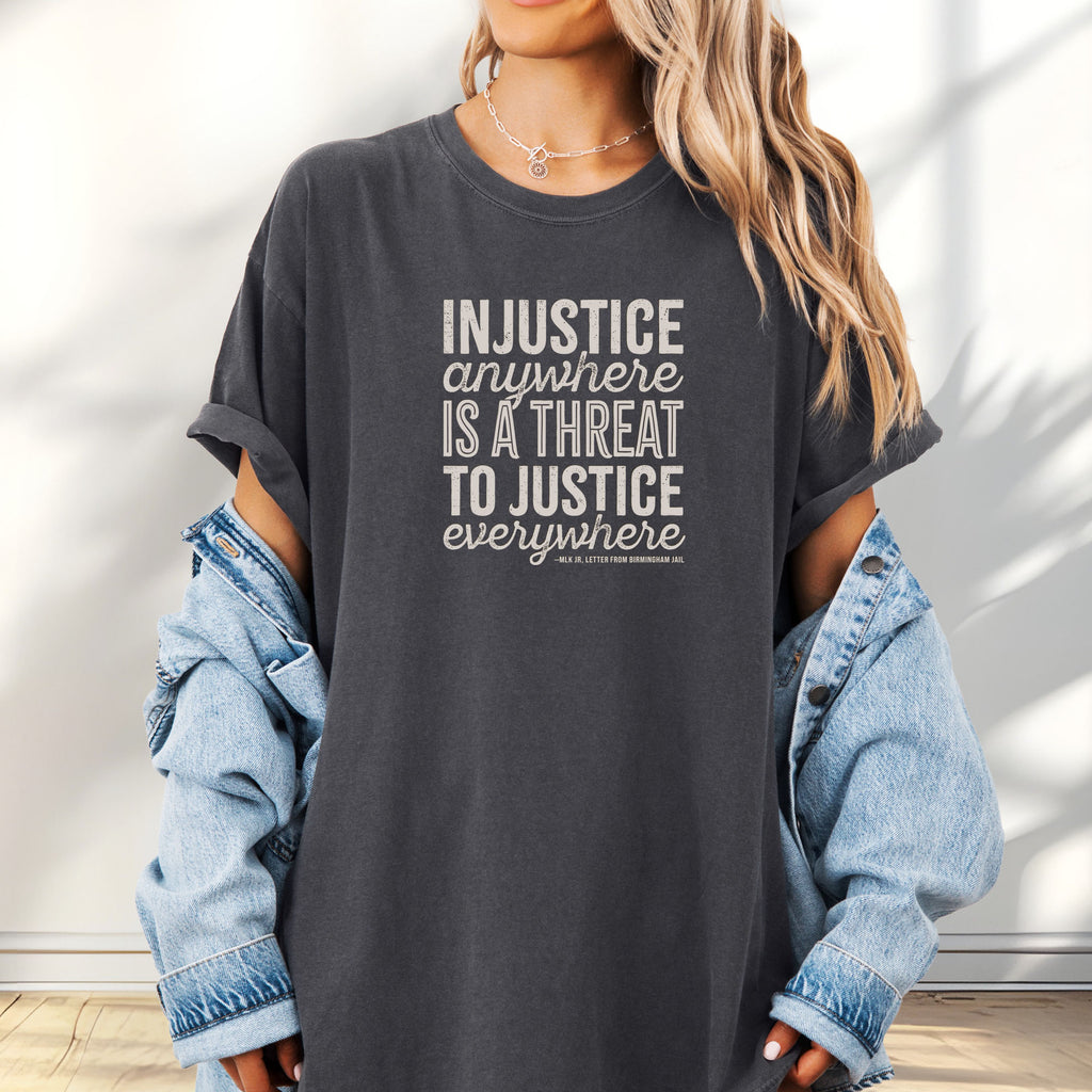 Female model wearing oversized pepper t-shirt with bold text reading “Injustice anywhere is a threat to justice everywhere” quote from Martin Luther King Jr, MLK Jr, Letter from Birmingham jail — civil rights protest apparel for activists.