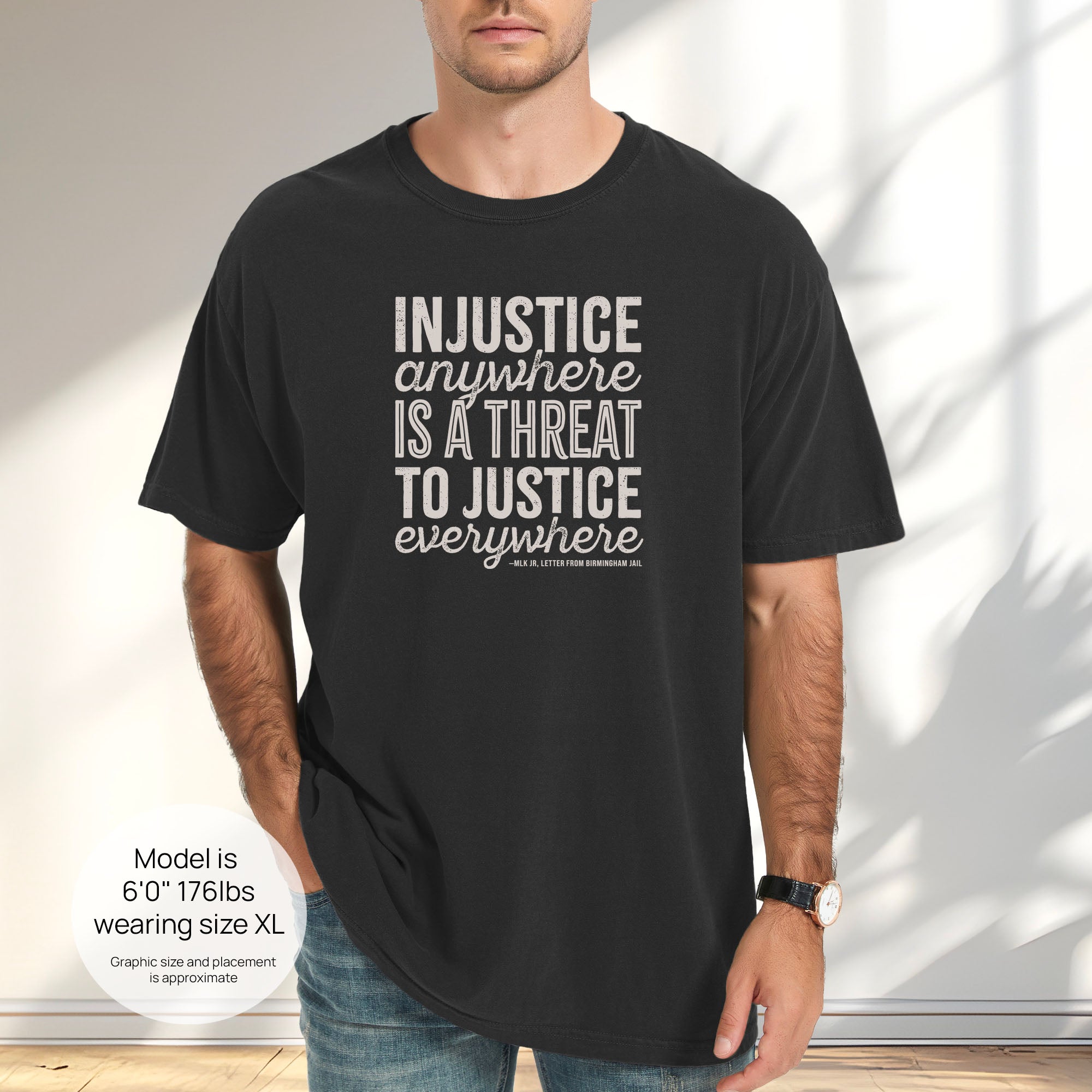 Male model wearing black t-shirt with bold text reading “Injustice anywhere is a threat to justice everywhere” quote from Martin Luther King Jr, MLK Jr, Letter from Birmingham jail — civil rights protest apparel for activists. Includes size and fit information for the model who is 6 feet 0 inches, 176 pounds, and wearing a size XL shirt.
