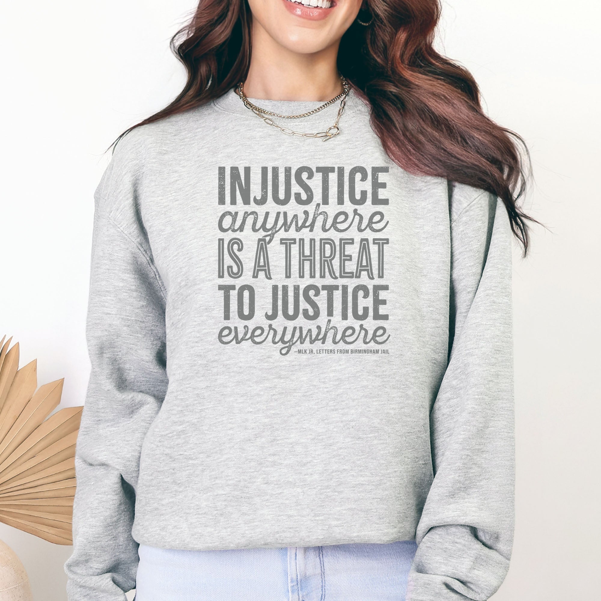 Female model wearing grey sweatshirt with bold text reading “Injustice anywhere is a threat to justice everywhere” quote from Martin Luther King Jr, MLK Jr, Letters from Birmingham jail — civil rights protest apparel for activists.