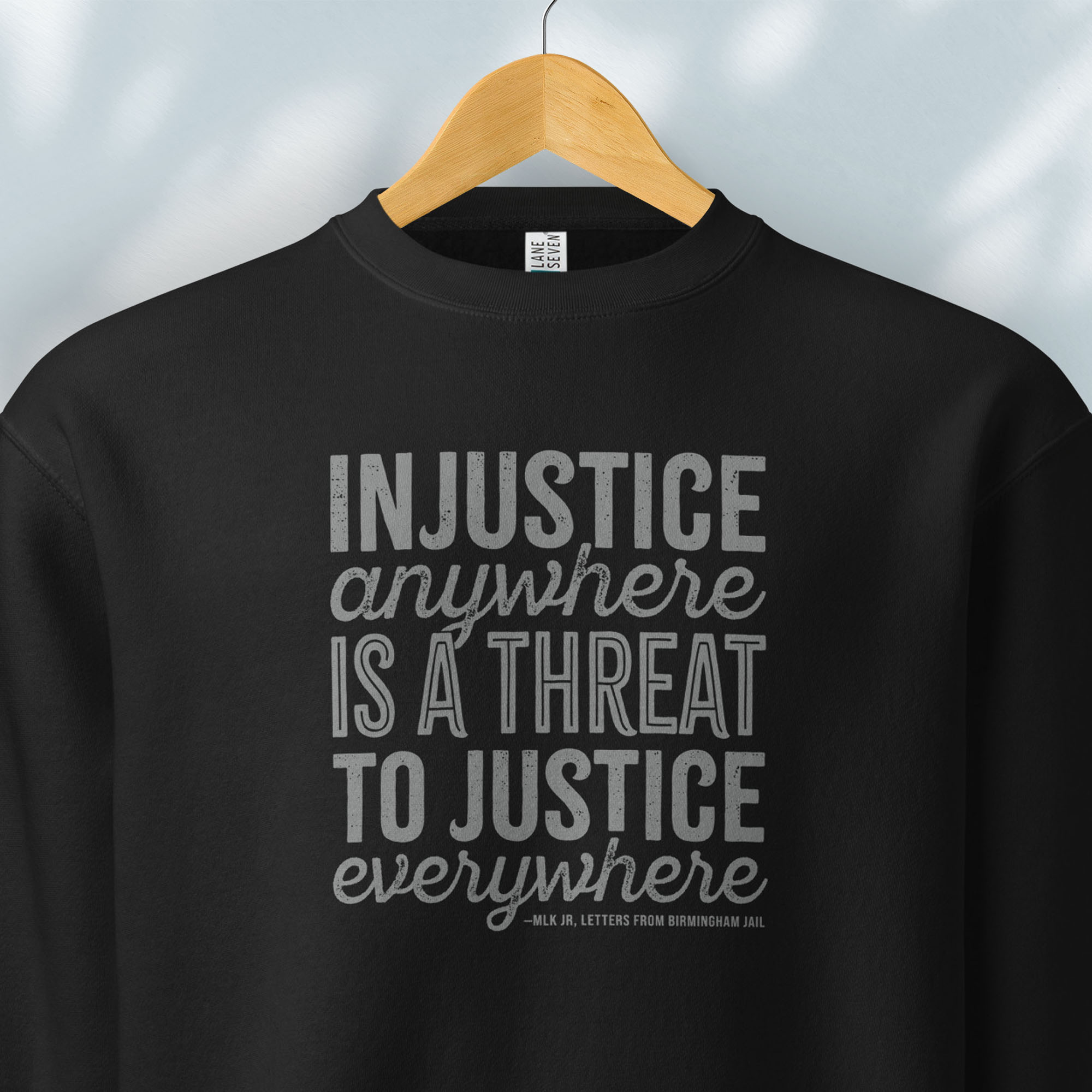 Hanging black sweatshirt with bold text reading “Injustice anywhere is a threat to justice everywhere” quote from Martin Luther King Jr, MLK Jr, Letters from Birmingham jail — civil rights protest apparel for activists.