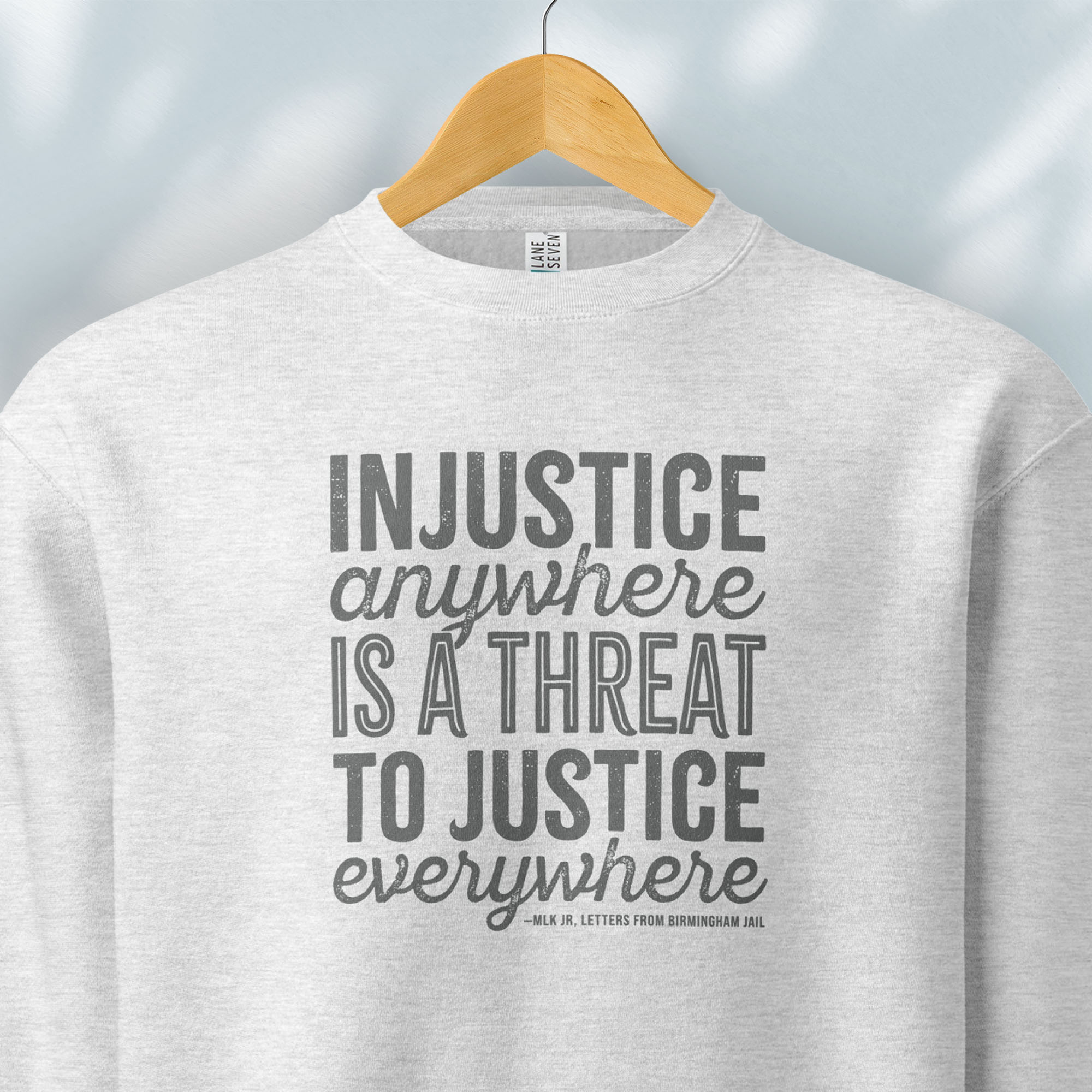Hanging grey sweatshirt with bold text reading “Injustice anywhere is a threat to justice everywhere” quote from Martin Luther King Jr, MLK Jr, Letters from Birmingham jail — civil rights protest apparel for activists.