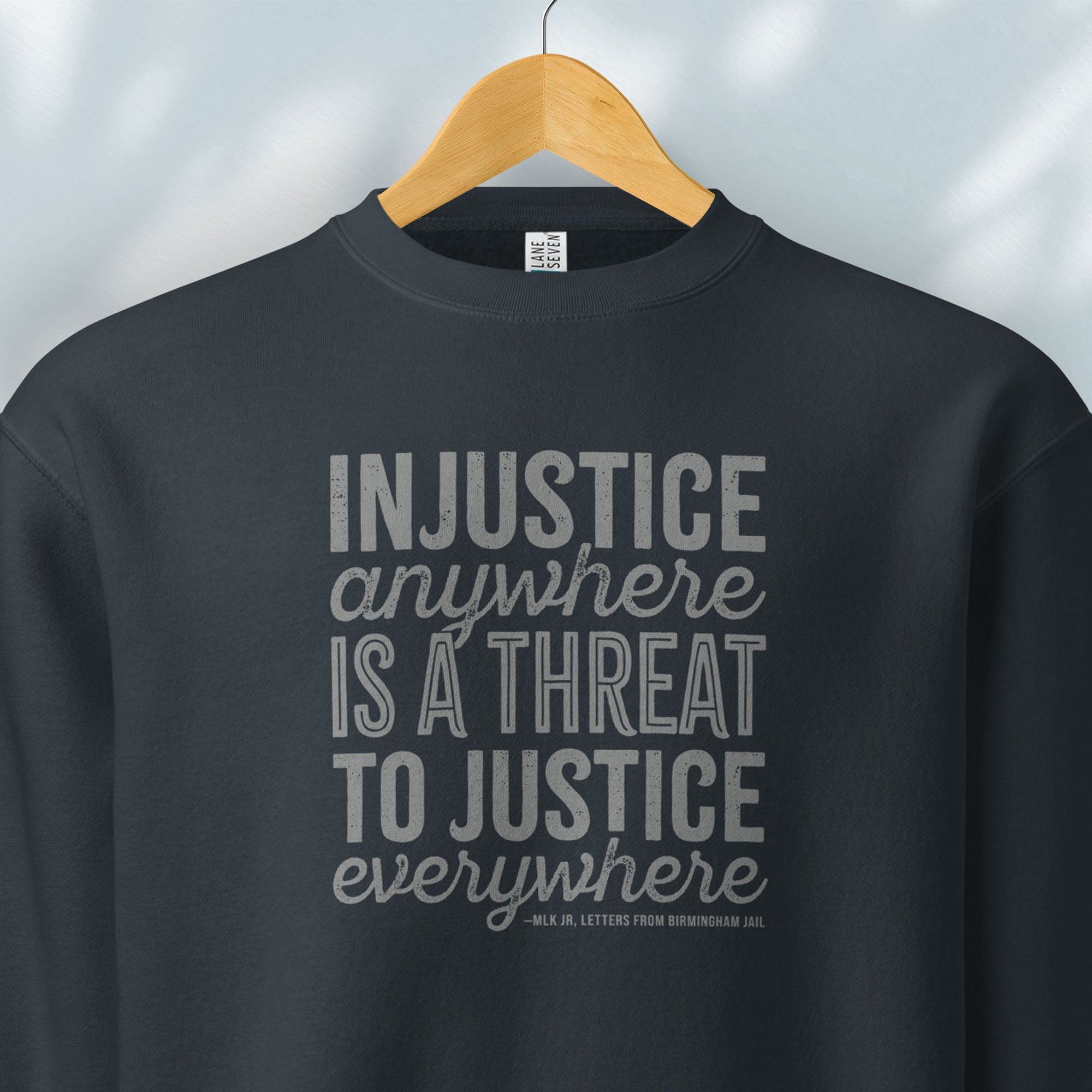 Hanging navy sweatshirt with bold text reading “Injustice anywhere is a threat to justice everywhere” quote from Martin Luther King Jr, MLK Jr, Letters from Birmingham jail — civil rights protest apparel for activists.