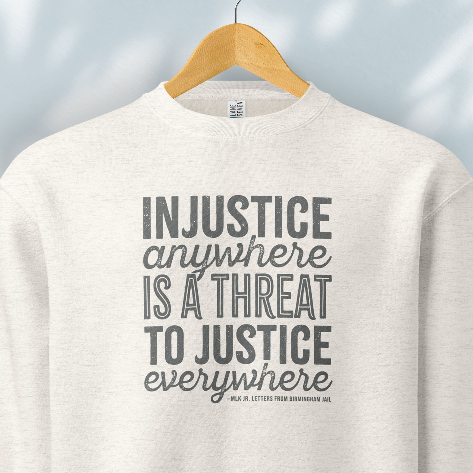Hanging oatmeal sweatshirt with bold text reading “Injustice anywhere is a threat to justice everywhere” quote from Martin Luther King Jr, MLK Jr, Letters from Birmingham jail — civil rights protest apparel for activists.