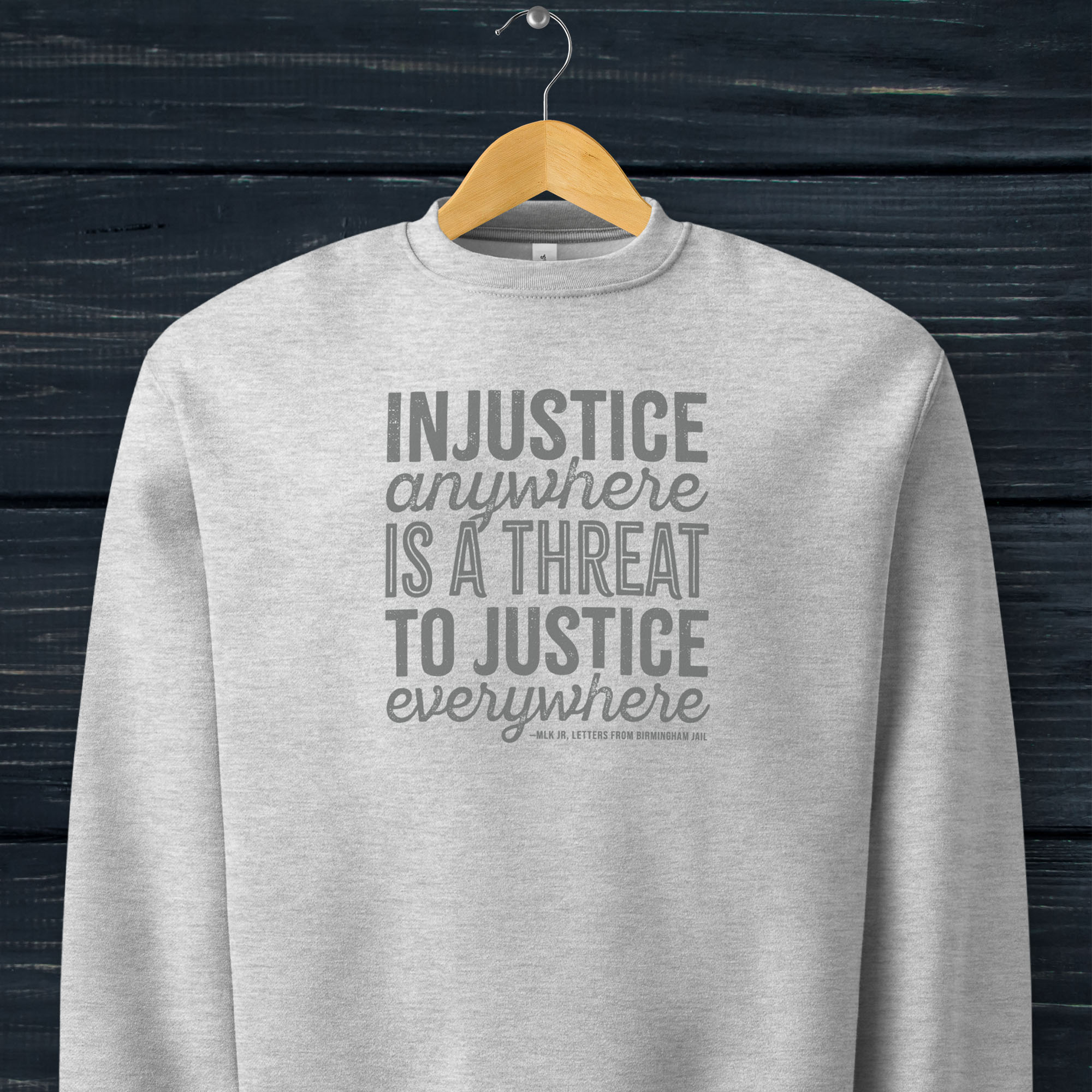Athletic heather grey sweatshirt with bold text reading “Injustice anywhere is a threat to justice everywhere” quote from Martin Luther King Jr, MLK Jr, Letters from Birmingham jail — civil rights protest apparel for activists. Hanging on a hanger.