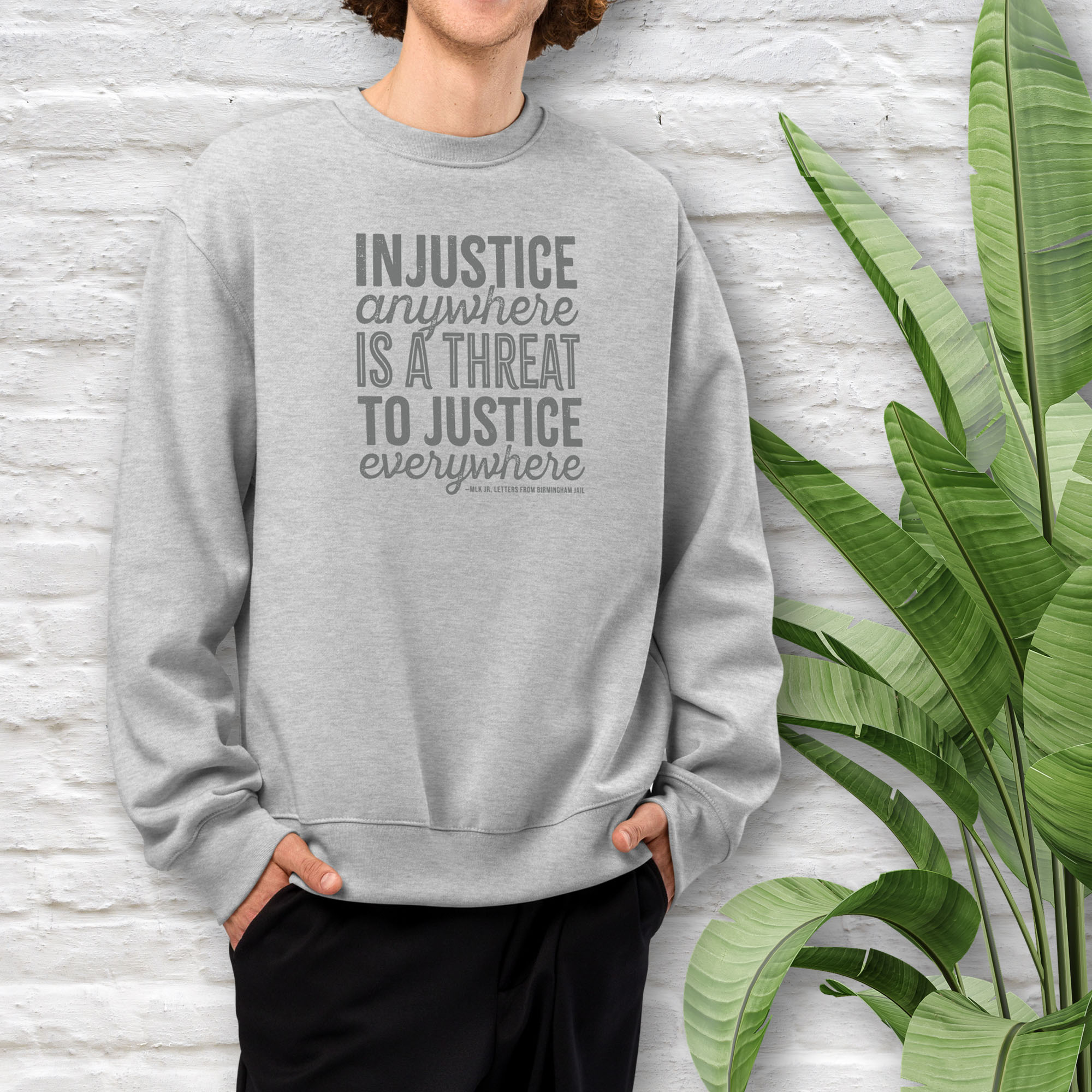 Male model wearing athletic heather grey sweatshirt with bold text reading “Injustice anywhere is a threat to justice everywhere” quote from Martin Luther King Jr, MLK Jr, Letters from Birmingham jail — civil rights protest apparel for activists.
