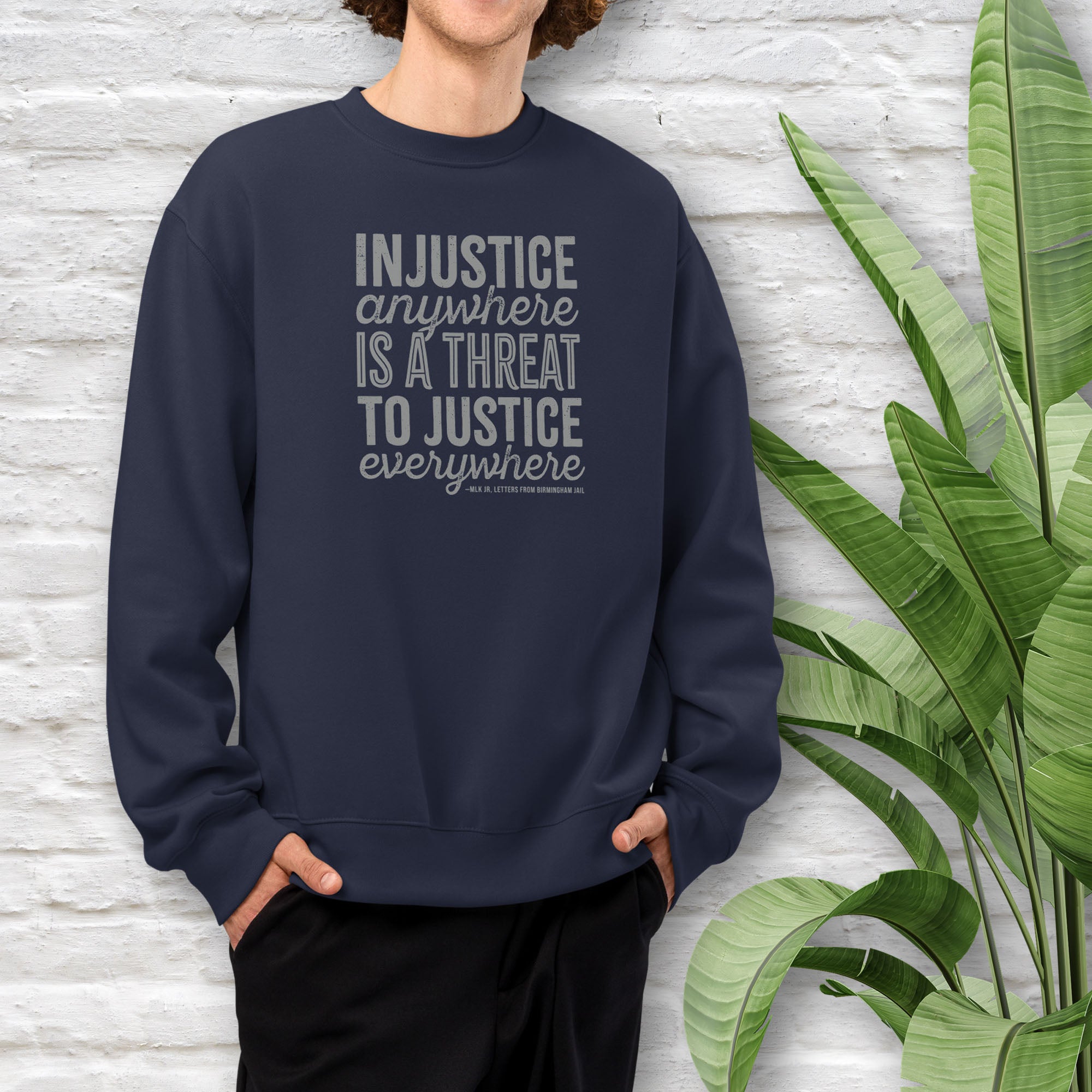 Male model wearing navy sweatshirt with bold text reading “Injustice anywhere is a threat to justice everywhere” quote from Martin Luther King Jr, MLK Jr, Letters from Birmingham jail — civil rights protest apparel for activists.