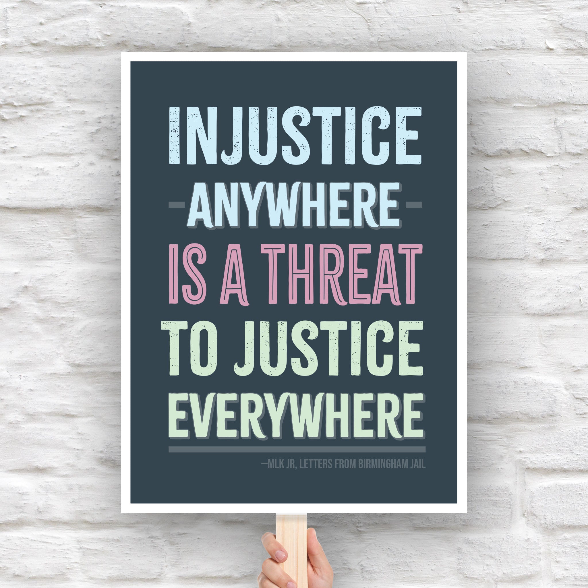 Protest sign with quote from Martin Luther King Jr that reads "injustice anywhere is a threat to justice everywhere" in colorful bold distressed text.